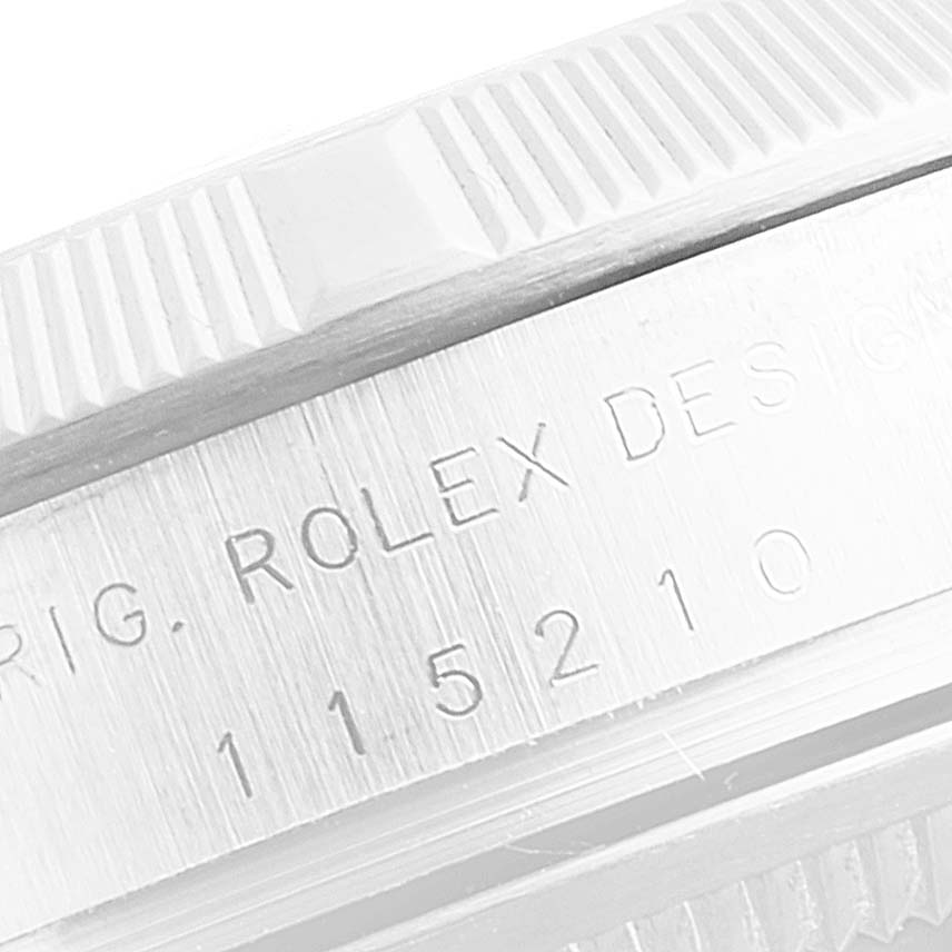 The image shows a close-up of the side of a Rolex Date 115210 Men's Stainless Steel Blue Dial 115210 Men's Stainless Steel Blue Dial model watch, highlighting the engraved serial number and fluted bezel.