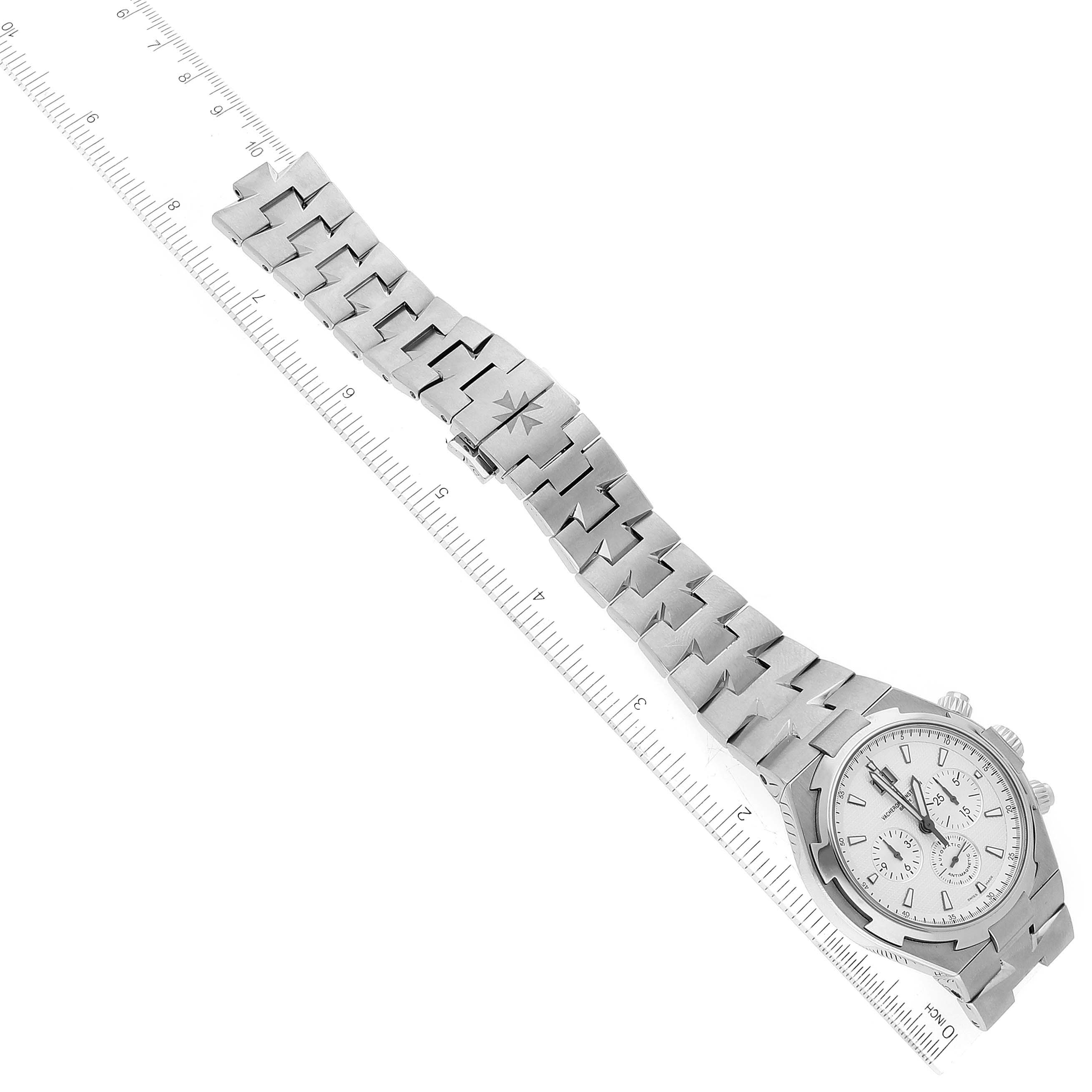 The Vacheron Constantin Overseas 49150/B01A-9095 Men's Stainless Steel Silver Dial 49150/B01A-9095 Men's Stainless Steel Silver Dial watch is shown from an overhead angle, displaying the dial and full length of the bracelet alongside a ruler for scale.