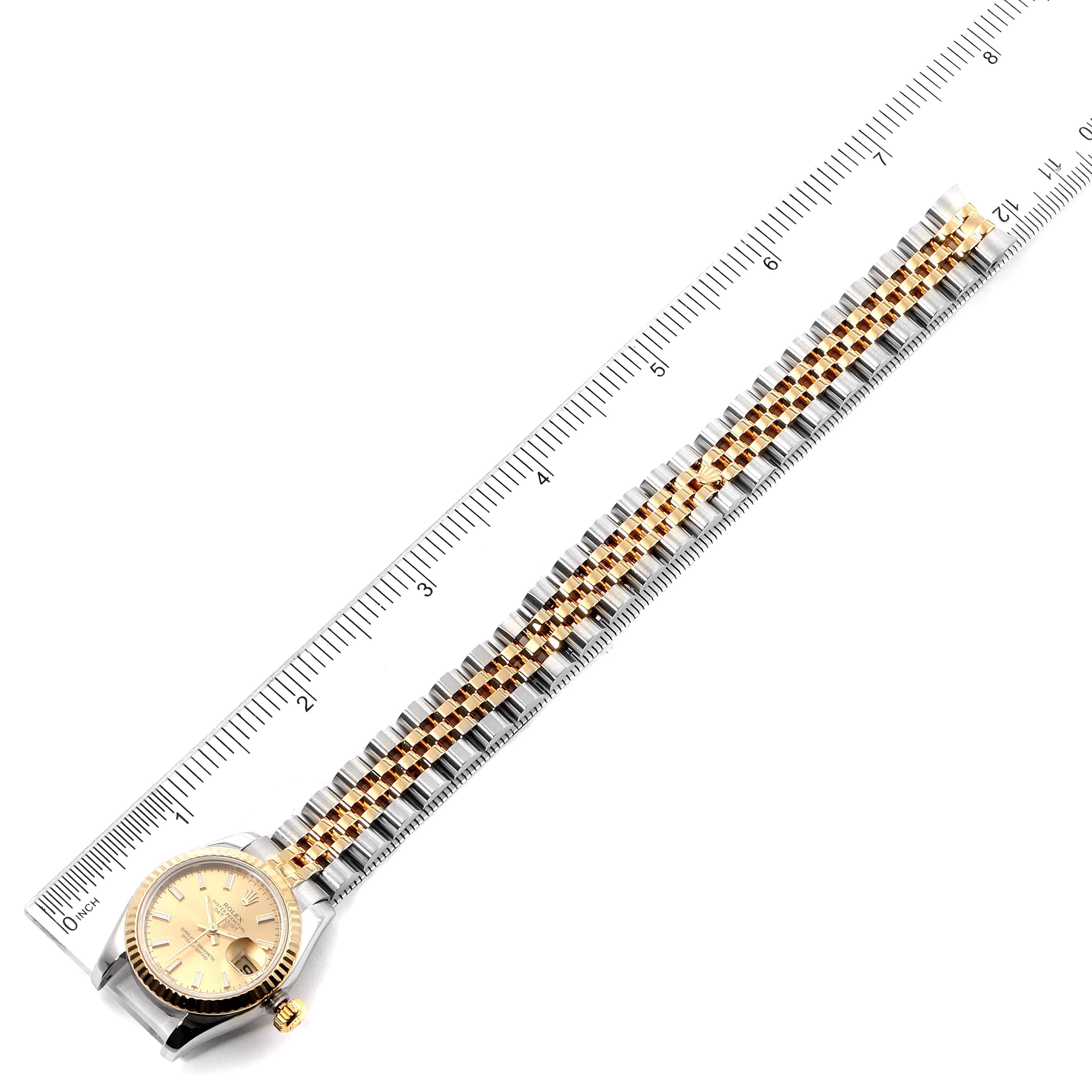 The Rolex Datejust 179173 Women's Steel and Gold (two tone) Champagne Dial 179173 Women's Steel and Gold (two tone) Champagne Dial watch is shown from a top-down angle, displaying its face, bezel, and full linked bracelet, with a ruler alongside for scale.