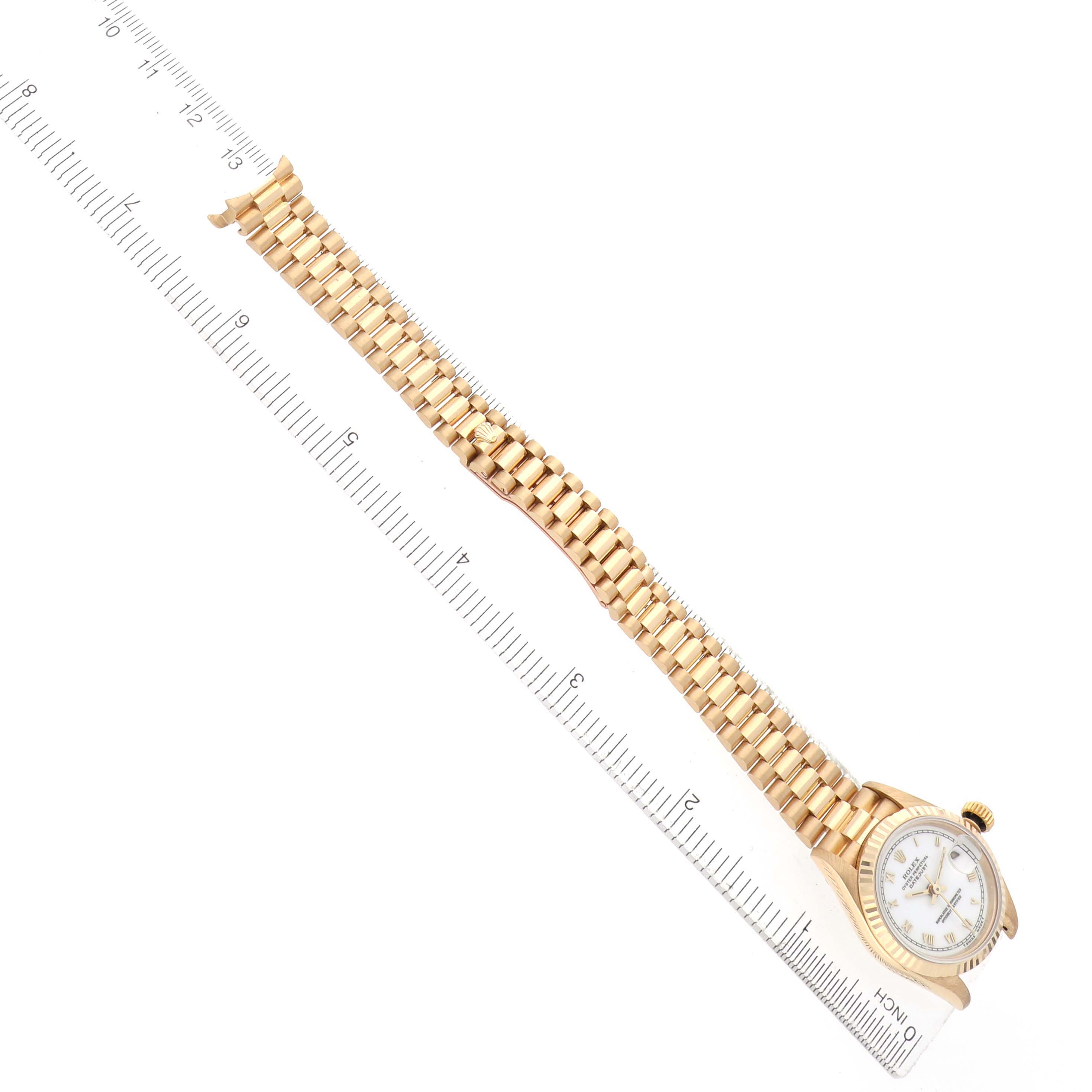 The Rolex Datejust 69178 Women's Yellow Gold White Dial watch is displayed from a top-down angle, showing the full bracelet and face alongside a ruler for scale.