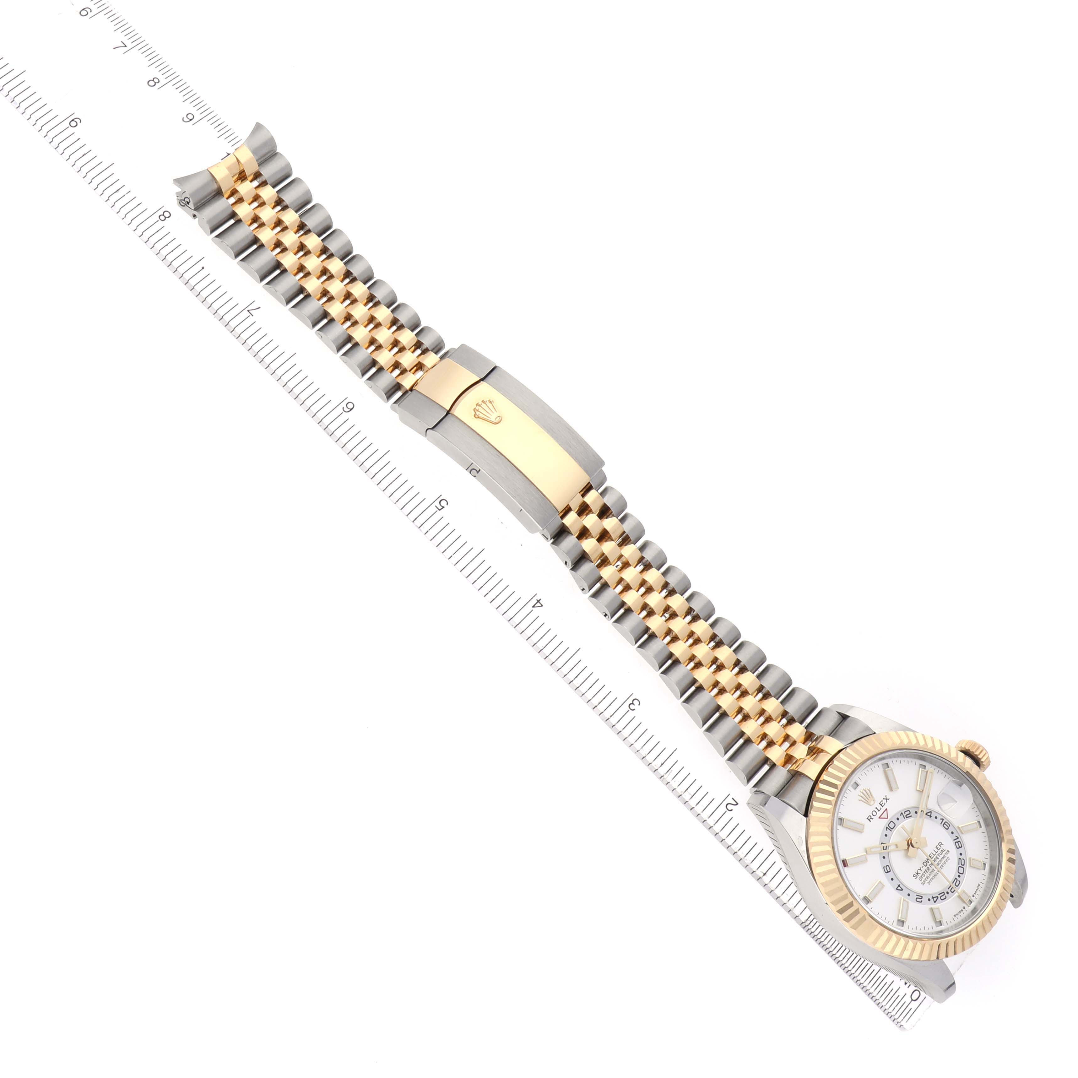 The Rolex Sky-Dweller 336933 Men's Steel and Gold (two tone) Silver Dial watch is shown from an angled top view, displaying the face, bracelet, and clasp with a ruler beside it.