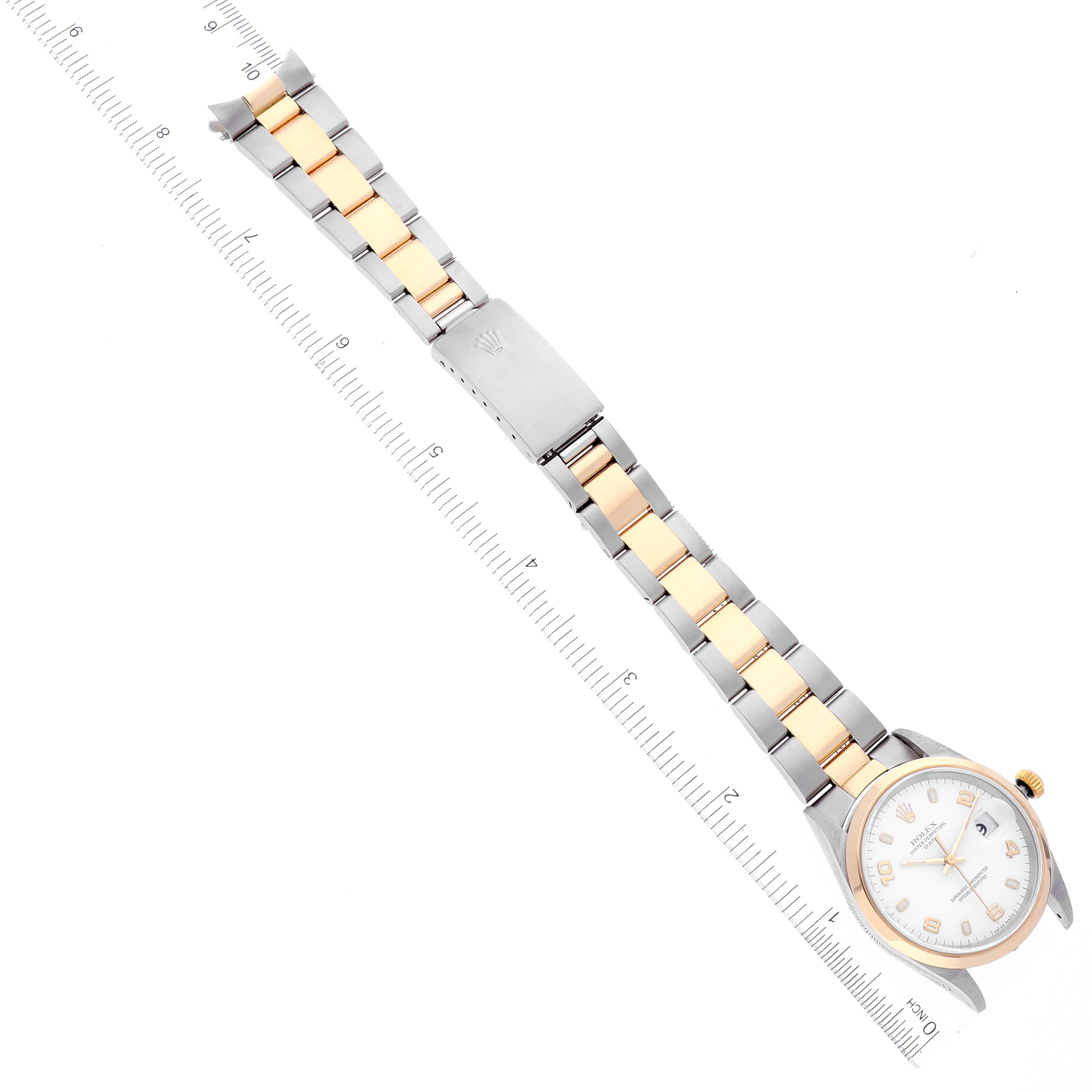 The image shows a Rolex Date 15203 Men's Steel and Gold (two tone) White Dial 15203 Men's Steel and Gold (two tone) White Dial model watch laid flat, perpendicular to a measuring ruler, showcasing its face, bezel, and bracelet.