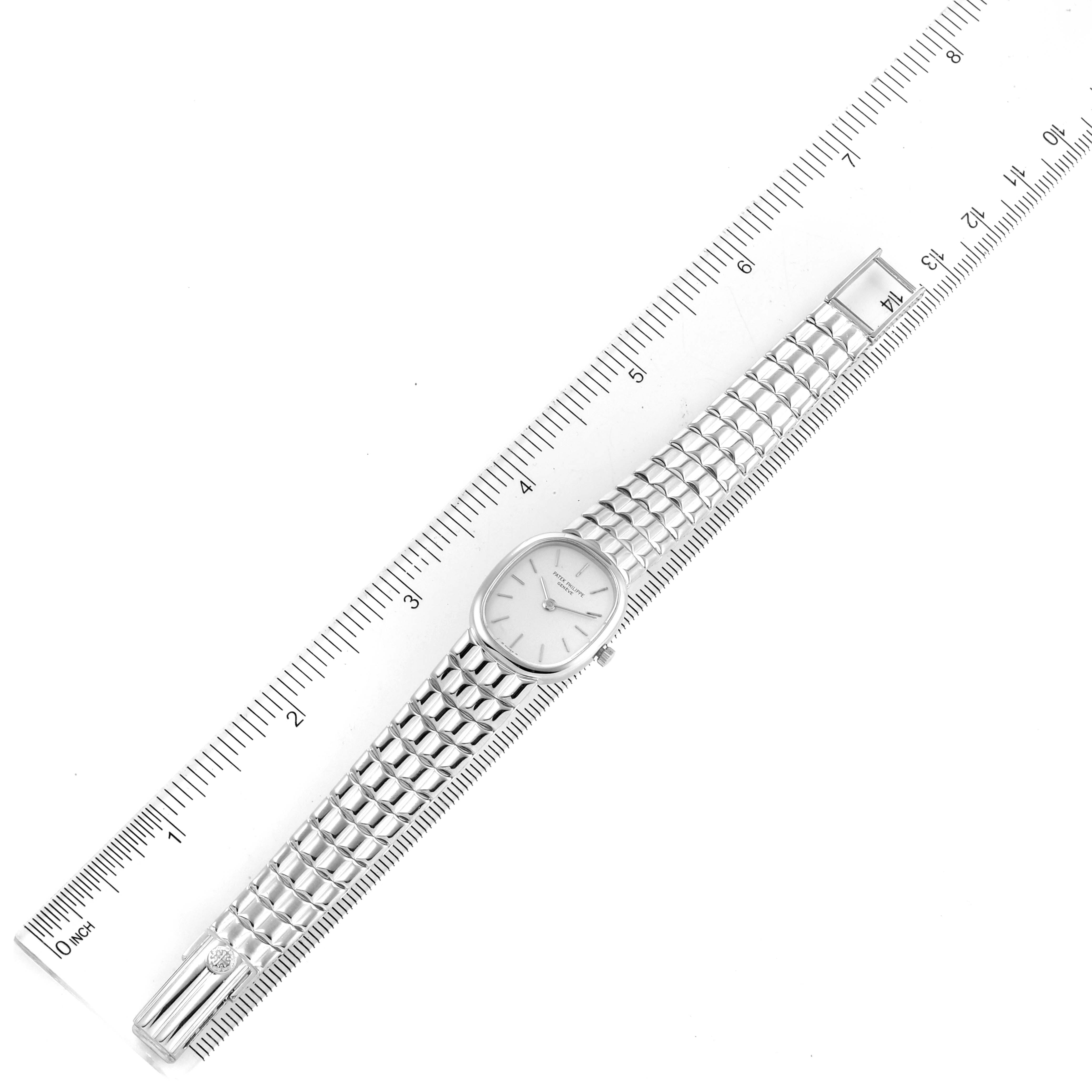The image shows a top view of a Patek Philippe Golden Ellipse 4764/15 Women's White Gold Silver Dial 4764/15 Women's White Gold Silver Dial watch with its band extended alongside a ruler.