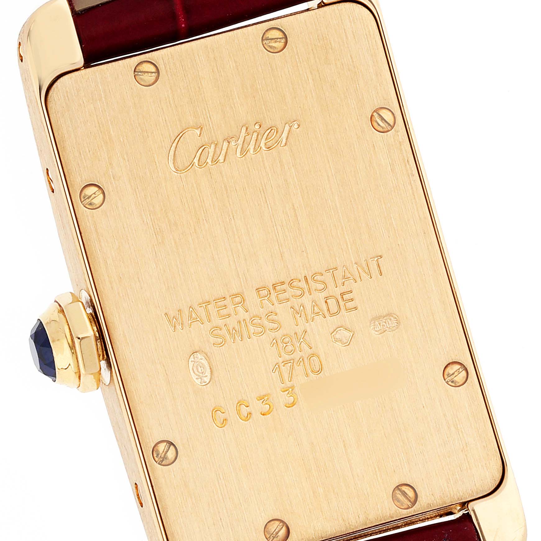This image shows the back case of a Cartier Tank Americaine W2601556 Women's Yellow Gold Silver Dial W2601556 Women's Yellow Gold Silver Dial watch, displaying engravings and the crown with a gemstone.