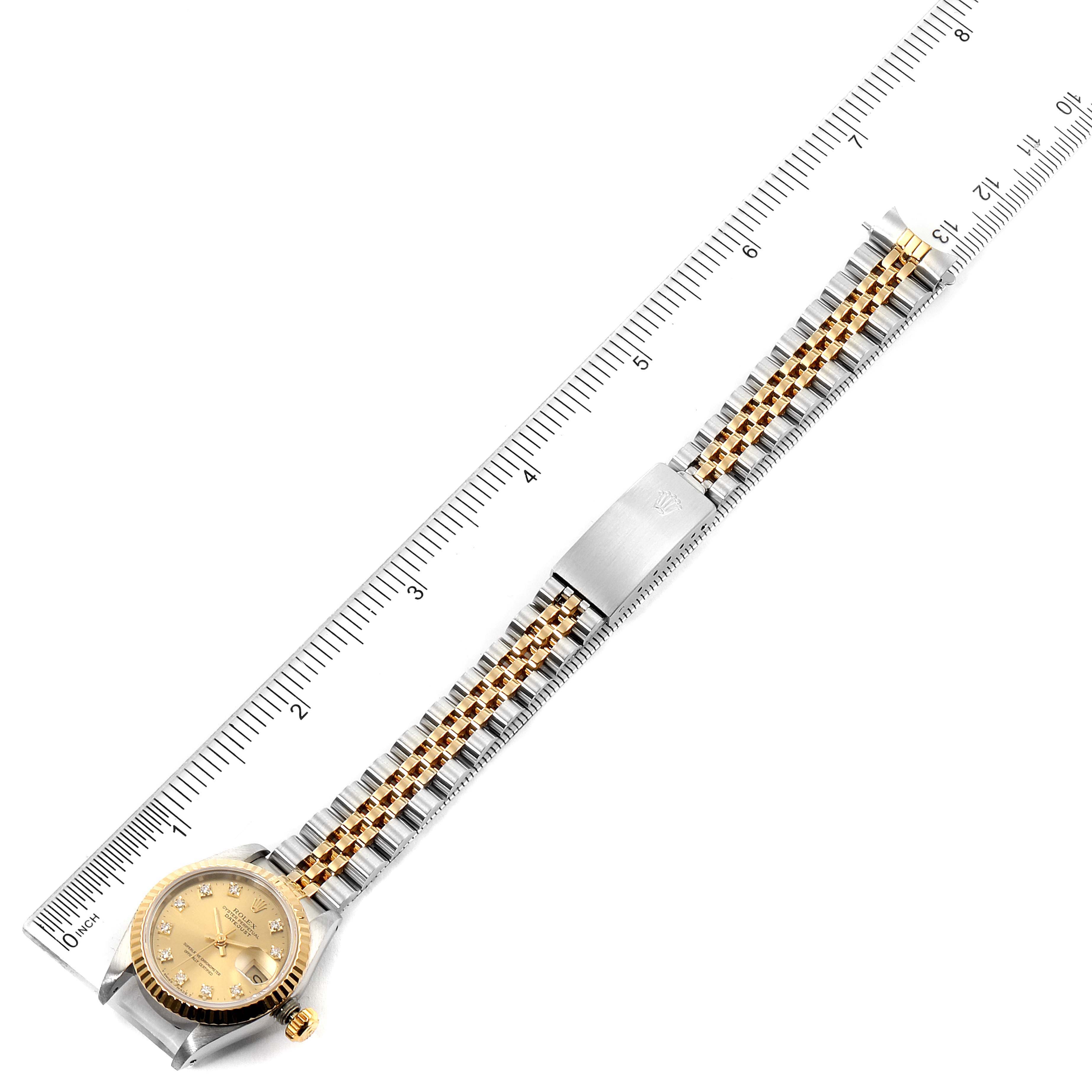 This Rolex Datejust 69173 Women's Steel and Gold (two tone) Champagne Dial 69173 Women's Steel and Gold (two tone) Champagne Dial watch is displayed flat alongside a ruler, showcasing the dial, bracelet, and clasp.