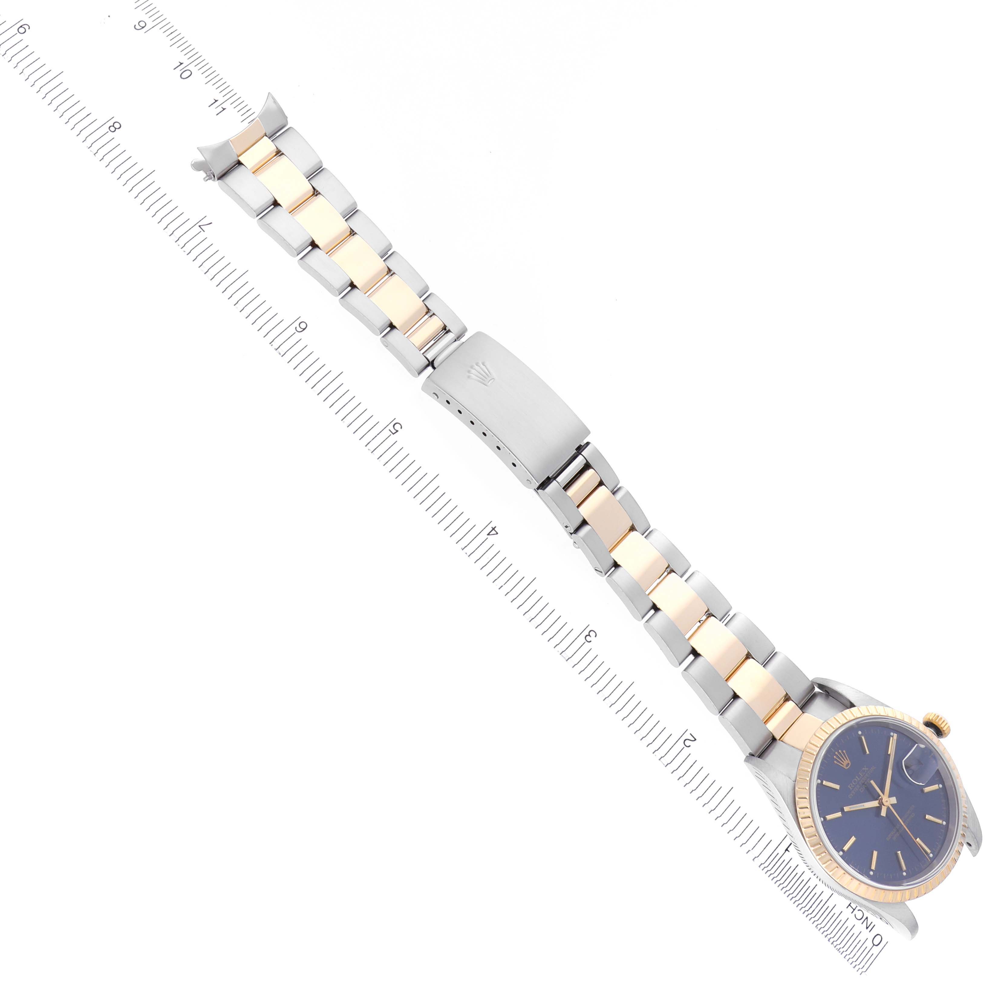 The Rolex Date 15223 Men's Steel and Gold (two tone) Blue Dial 15223 Men's Steel and Gold (two tone) Blue Dial watch is shown from a top-down angle, highlighting its bracelet and clasp alongside a ruler.