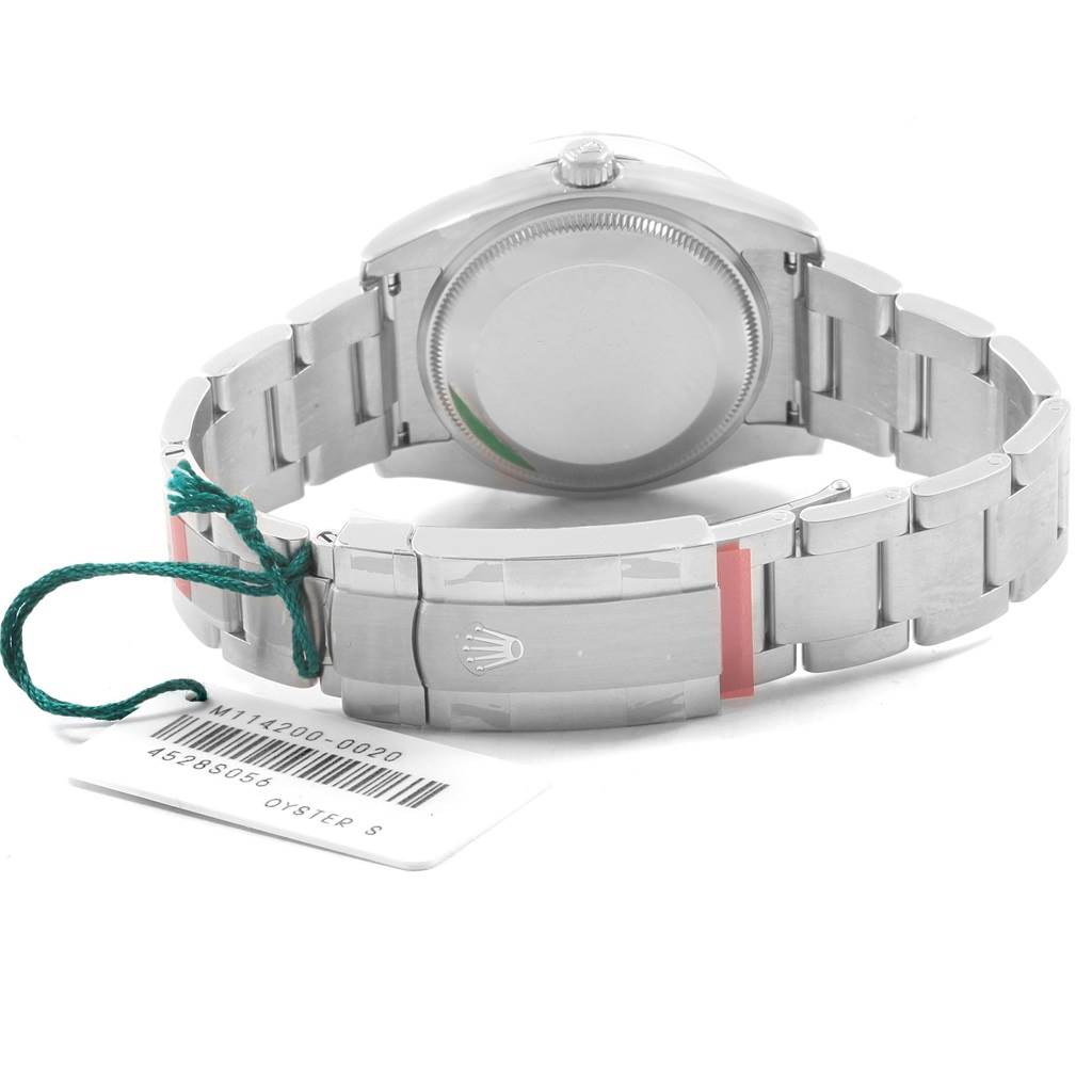 The image shows the back view of a Rolex Oyster Perpetual 114200 Men's Stainless Steel Burgundy Dial 114200 Men's Stainless Steel Burgundy Dial watch, focusing on the case back and the clasp with an attached tag.