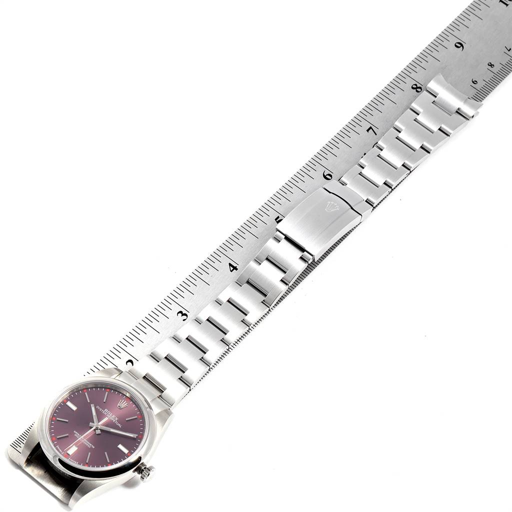 This image shows a top view of the Rolex Oyster Perpetual 114300 Men's Stainless Steel Burgundy Dial 114300 Men's Stainless Steel Burgundy Dial watch with a metal bracelet placed alongside a ruler.