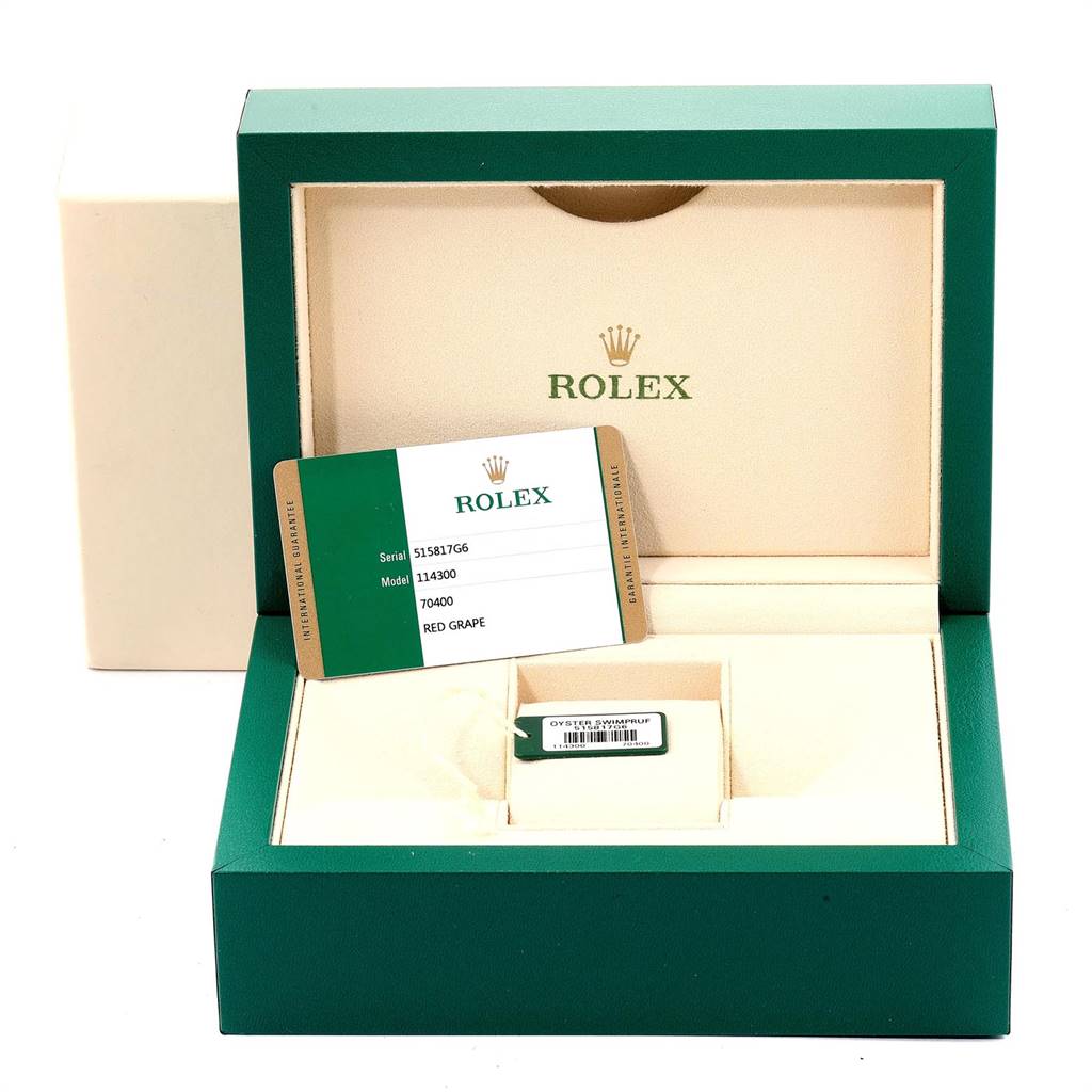 The image shows the open box and warranty card for a Rolex Oyster Perpetual 114300 Men's Stainless Steel Burgundy Dial 114300 Men's Stainless Steel Burgundy Dial model.