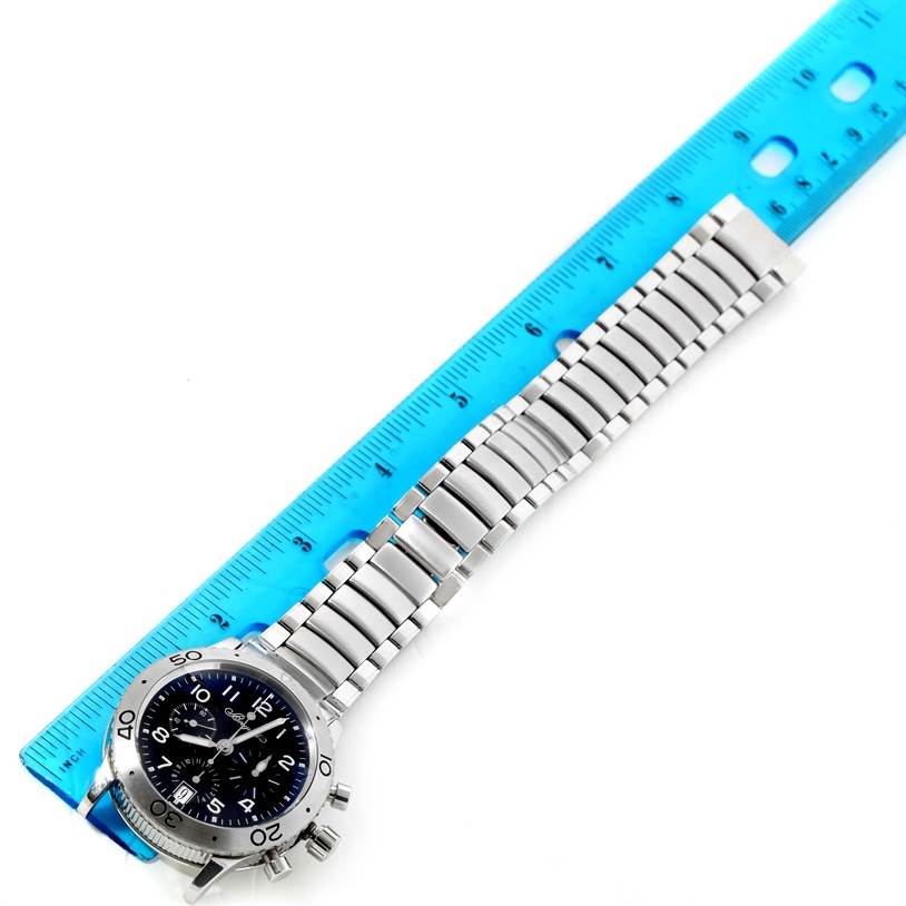 The image shows a Breguet Type XX - XXI - XXII 3820ST/H2/SW9 Men's Stainless Steel Black Dial 3820ST/H2/SW9 Men's Stainless Steel Black Dial watch with a steel bracelet laid next to a blue ruler, viewed from above.