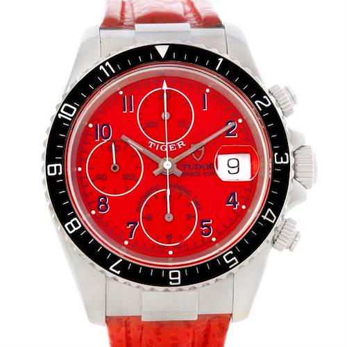 The watch, a Tiger model by Tudor, is shown from the front, displaying the red dial, chronographs, and part of the strap.