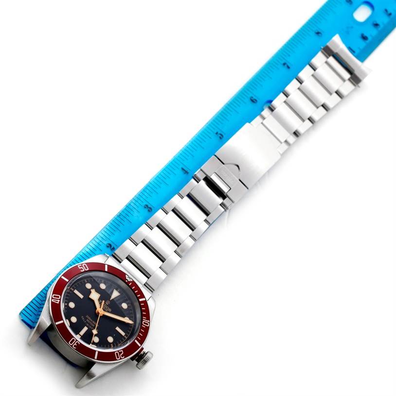 The image shows a top-down view of the Tudor Heritage Black Bay 79220 Men's Stainless Steel Black Dial 79220 Men's Stainless Steel Black Dial watch with a metal bracelet next to a blue ruler.