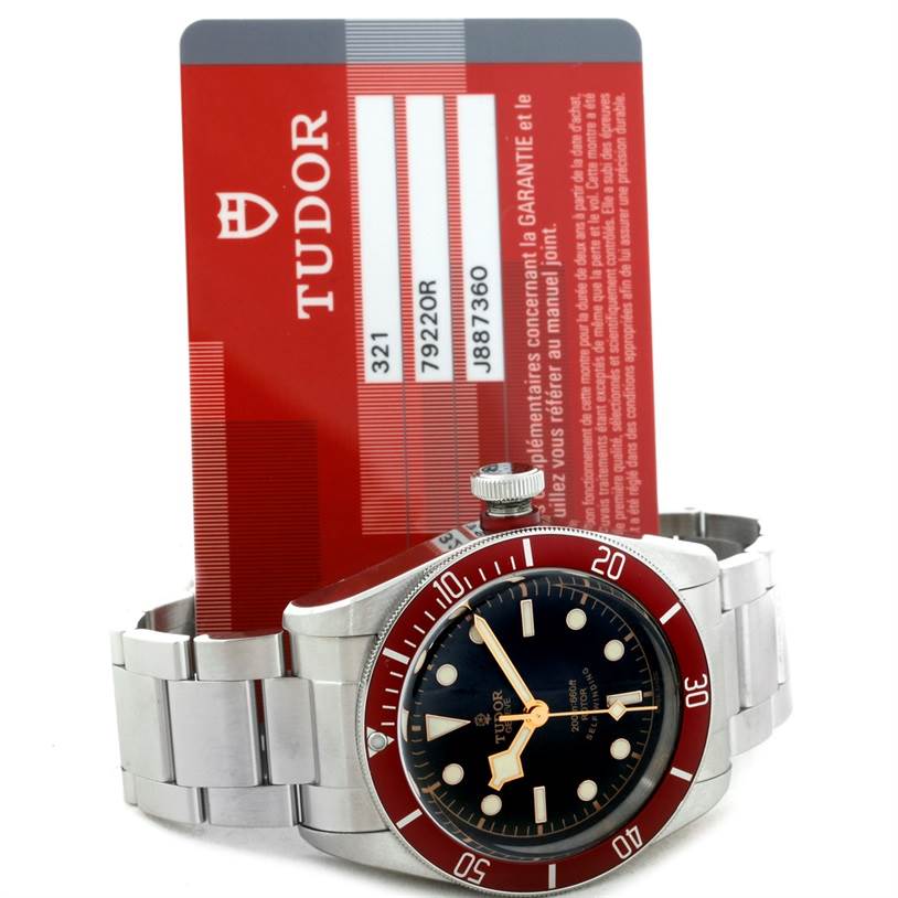 The image shows a Tudor Heritage Black Bay 79220 Men's Stainless Steel Black Dial 79220 Men's Stainless Steel Black Dial watch front view, including its face, bezel, and part of the bracelet, alongside its guarantee card.