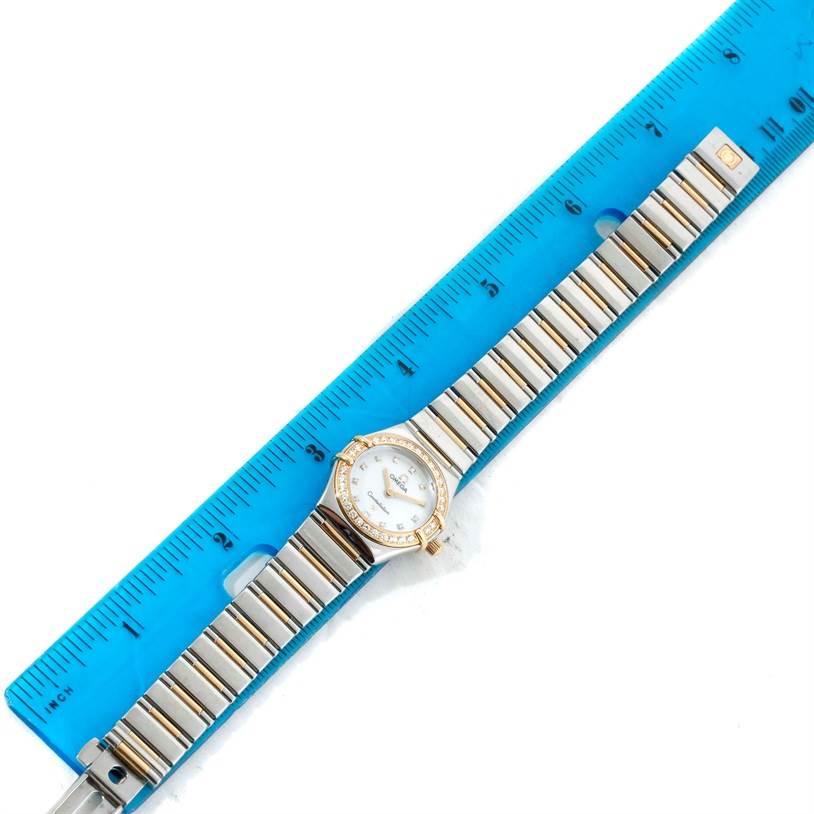The Omega 1365.75.00 Women's Steel and Gold (two tone) Mother of Pearl Dial 1365.75.00 Women's Steel and Gold (two tone) Mother of Pearl Dial Constellation Mini Steel Yellow Gold Diamond Watch 1365.75.00 is displayed flat from above with a ruler for scale, showing the dial, bezel, and bracelet.