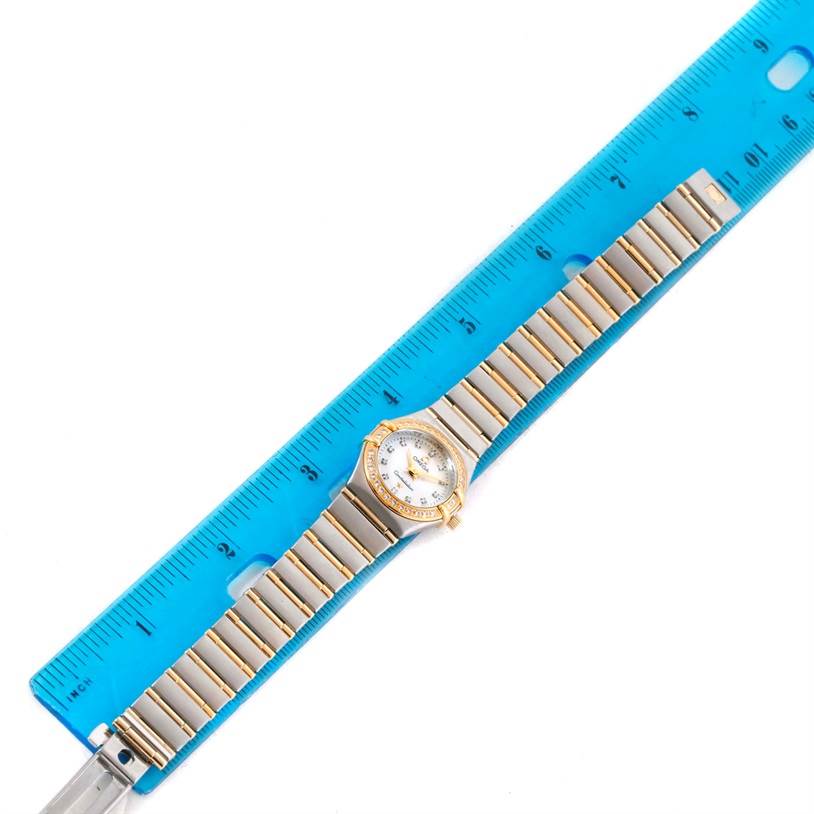 The image shows an Omega 1267.75.00 Women's Steel and Gold (two tone) Mother of Pearl Dial 1267.75.00 Women's Steel and Gold (two tone) Mother of Pearl Dial Constellation My Choice Mini Steel Gold Diamond Watch 1267.75.00 laid flat beside a blue ruler for scale.