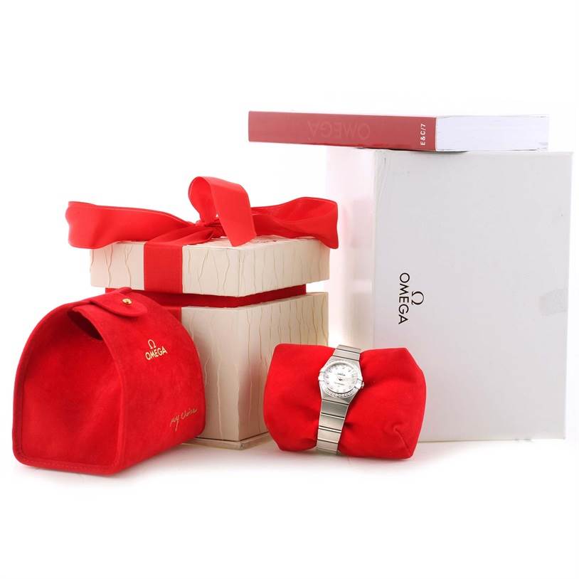 The image shows the Omega 123.15.27.60.55.002 Women's Stainless Steel Mother of Pearl Dial 123.15.27.60.55.002 Women's Stainless Steel Mother of Pearl Dial Constellation 27mm Diamond Ladies Watch model 123.15.27.60.55.002 with its packaging and accessories.