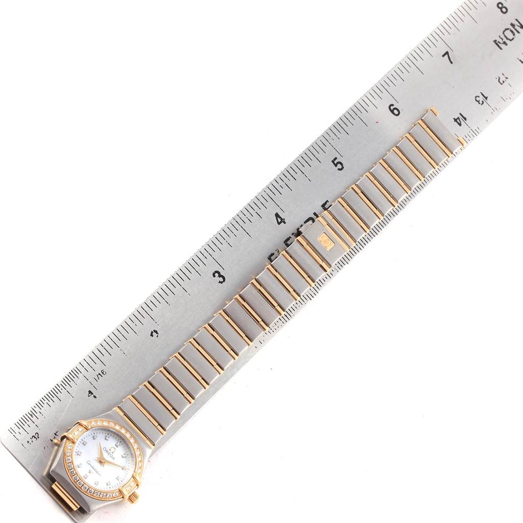 The image shows an Omega 1267.75.00 Women's Steel and Gold (two tone) Mother of Pearl Dial 1267.75.00 Women's Steel and Gold (two tone) Mother of Pearl Dial Constellation Mini Mother of Pearl Diamond Watch 1267.75.00 laying next to a ruler for size reference.