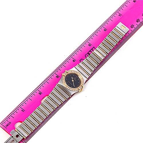 The Omega 1267.10.00 Women's Steel and Gold (two tone) Black Dial 1267.10.00 Women's Steel and Gold (two tone) Black Dial Constellation Diamond Mini 1267.10.00 watch is shown laid flat, with the entire bracelet and face visible, alongside a pink ruler for scale.