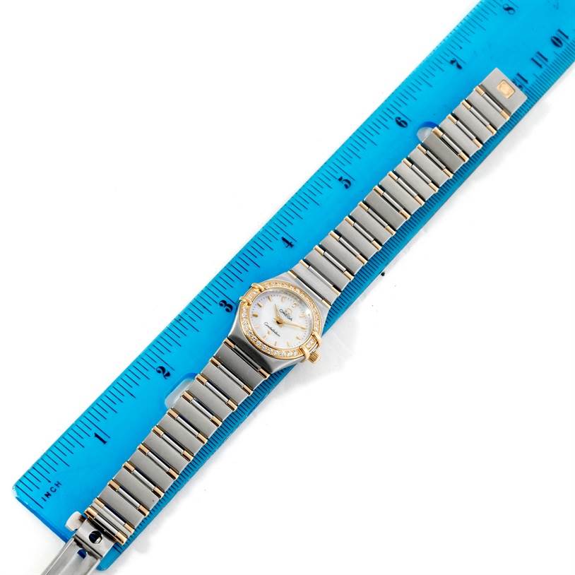 The Omega 56945066 Women's Steel and Gold (two tone) Mother of Pearl Dial 56945066 Women's Steel and Gold (two tone) Mother of Pearl Dial Constellation Mini Steel and Gold Diamond Watch is shown lying flat against a blue ruler, displaying the full bracelet and face.
