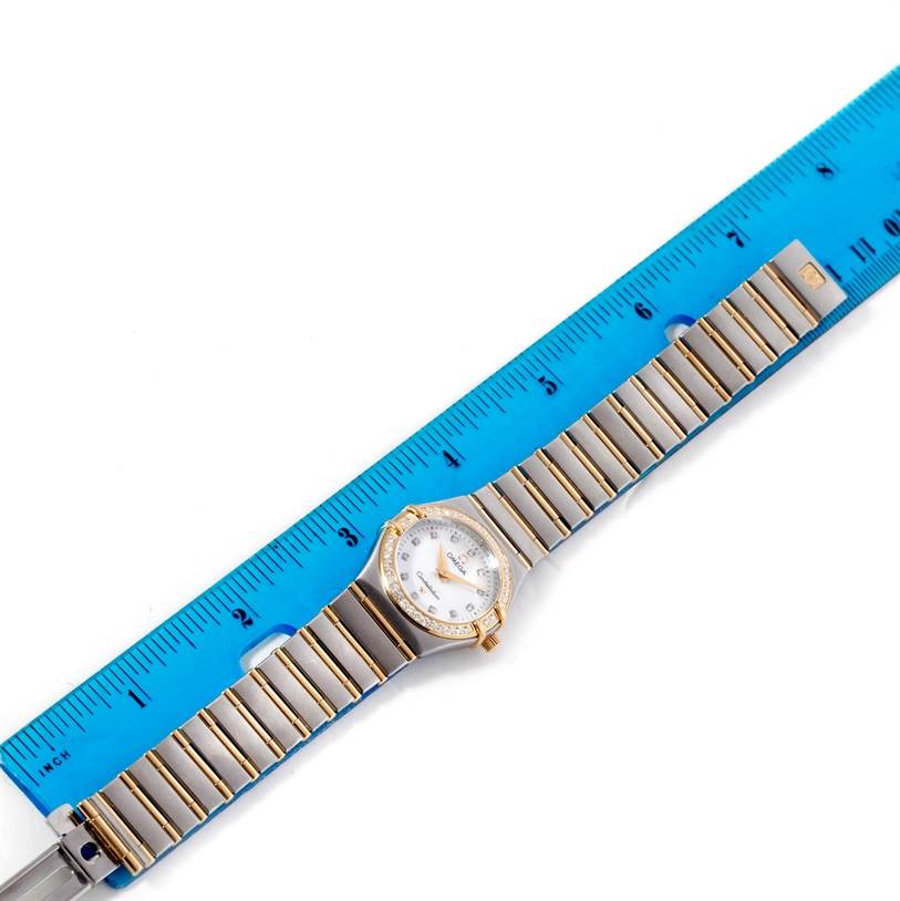 The image shows an Omega 1277.75.00 Women's Steel and Gold (two tone) Mother of Pearl Dial 1277.75.00 Women's Steel and Gold (two tone) Mother of Pearl Dial Constellation My Choice Steel Gold Diamond Watch 1277.75.00 laid flat next to a blue ruler for measurement.