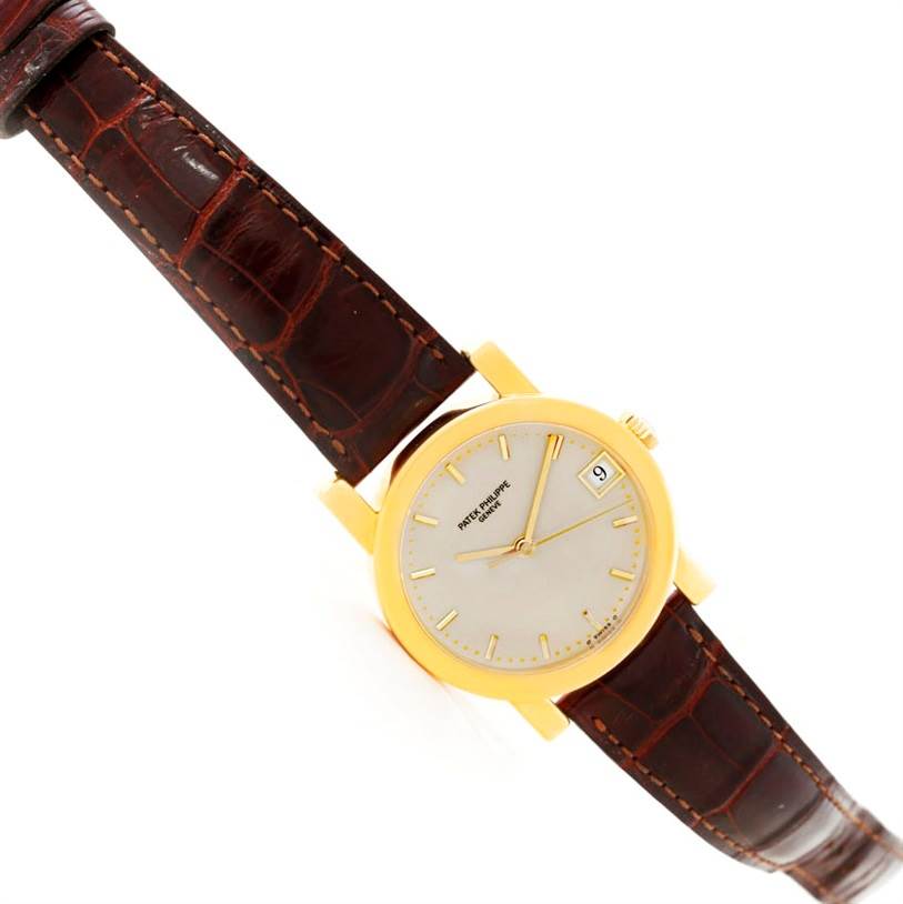 The image shows a Patek Philippe Calatrava 5012 Men's Yellow Gold Beige Dial 5012 Men's Yellow Gold Beige Dial watch at a slight angle, featuring its dial, leather strap, and gold casing.