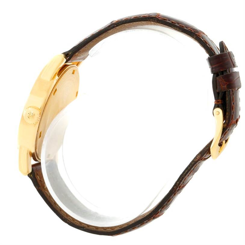 The image shows a side view of a Patek Philippe Calatrava 5012 Men's Yellow Gold Beige Dial 5012 Men's Yellow Gold Beige Dial watch, highlighting the case, crown, and leather strap.