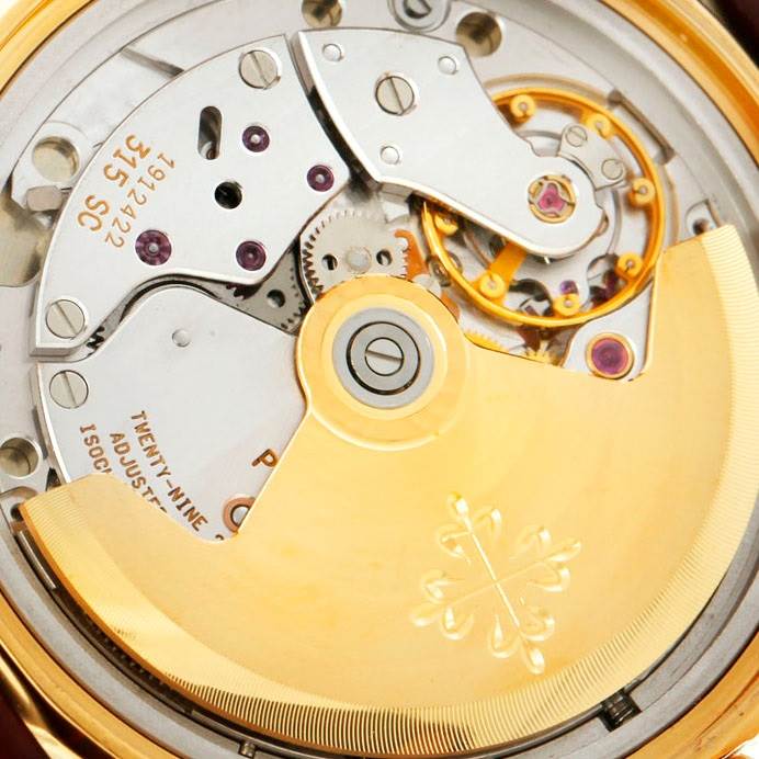 The image shows an angled close-up of the movement of a Patek Philippe Calatrava 5012 Men's Yellow Gold Beige Dial 5012 Men's Yellow Gold Beige Dial watch, highlighting its intricate mechanism and rotor.
