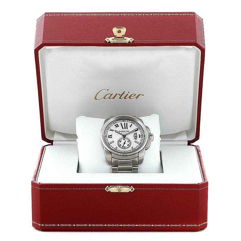 The Calibre de Cartier watch by Cartier is shown from a front angle in an open red and white box with gold accents.