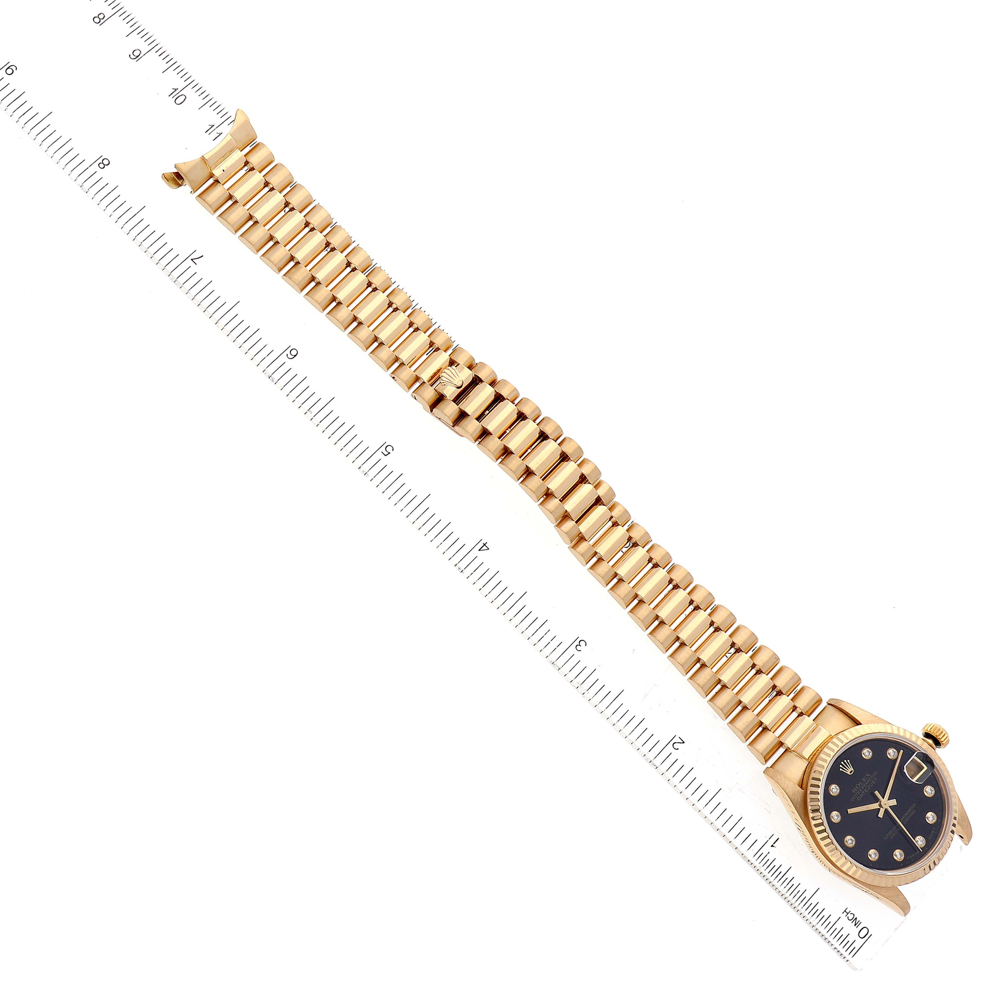 The image displays a Rolex President 68278G Women's Yellow Gold Black Dial 68278G Women's Yellow Gold Black Dial model watch lying flat, showcasing its face, bracelet, and a ruler nearby.