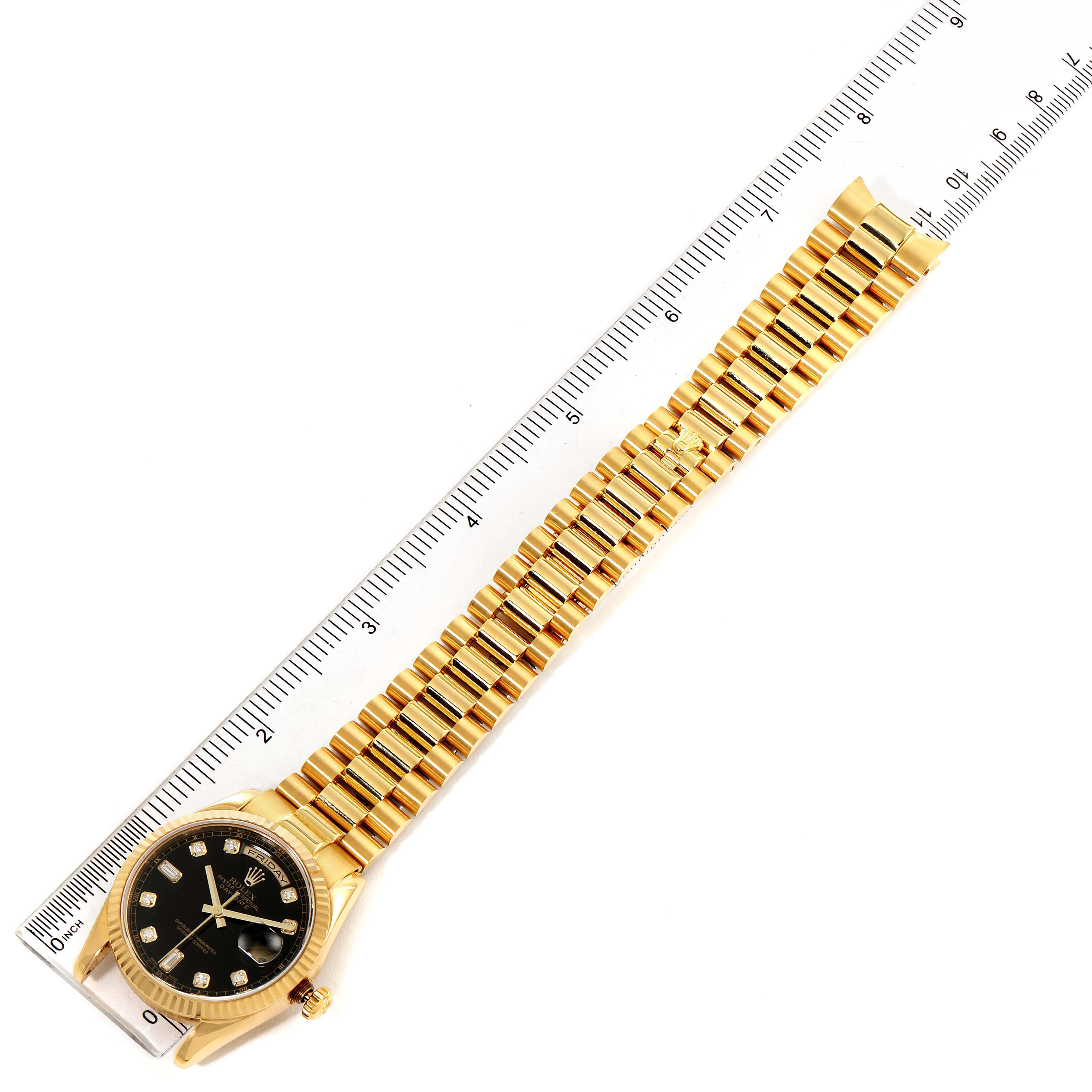 The Rolex President 118238 Men's Yellow Gold Black Dial 118238 Men's Yellow Gold Black Dial watch is shown from a top-down angle, displaying the face, bezel, and full gold bracelet next to a ruler.