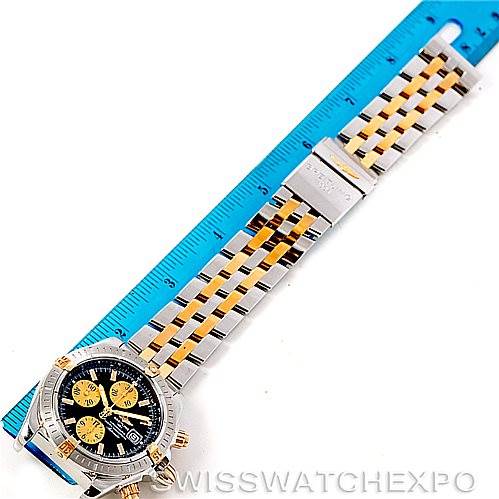 The image shows a top view of a Breitling Chronomat B13356 Men's Steel and Gold (two tone) Black Dial B13356 Men's Steel and Gold (two tone) Black Dial watch, highlighting the bracelet and face next to a blue ruler for scale.