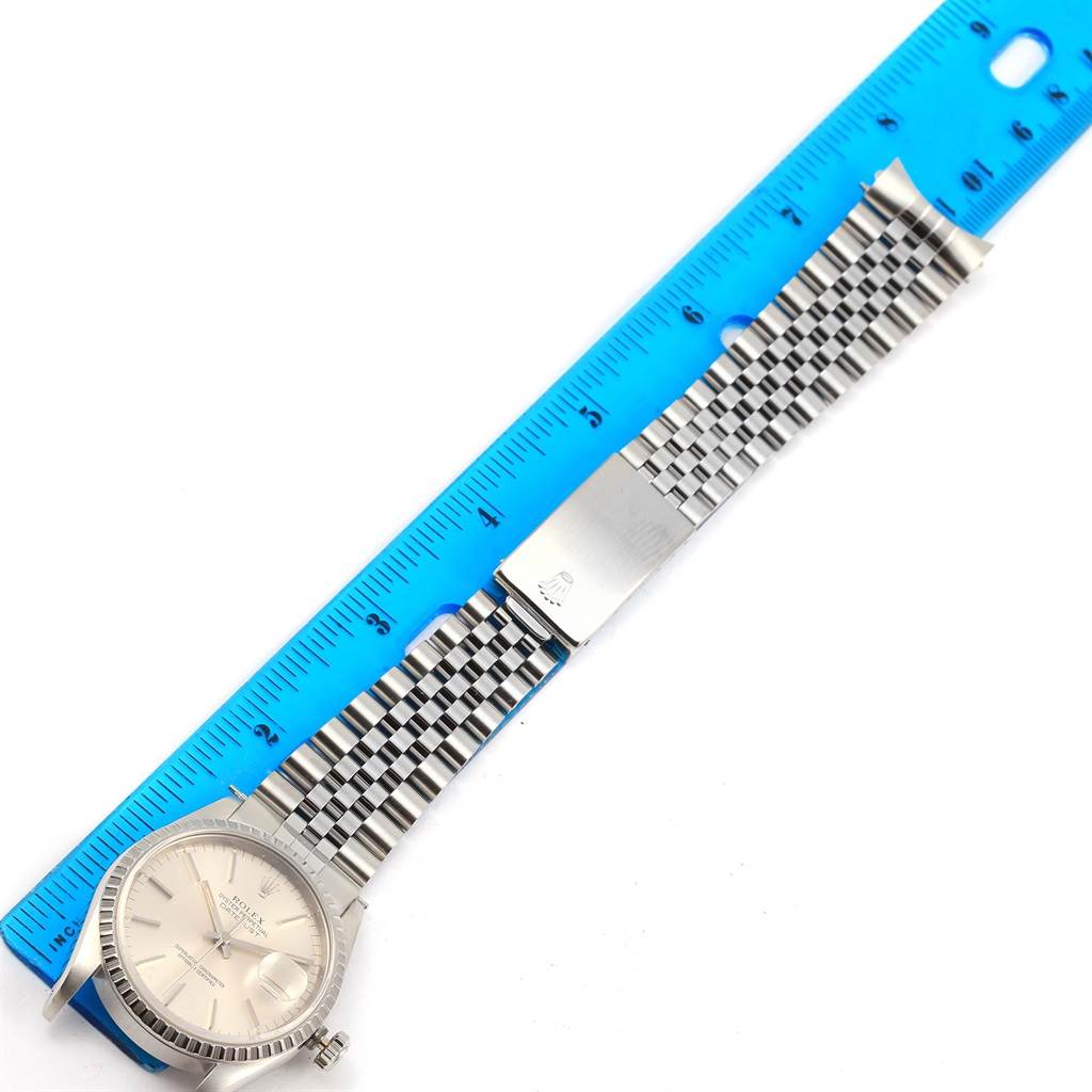 The image shows a top view of a Rolex Datejust 16220 Men's Stainless Steel Silver Dial 16220 Men's Stainless Steel Silver Dial watch with its band extended alongside a blue ruler.