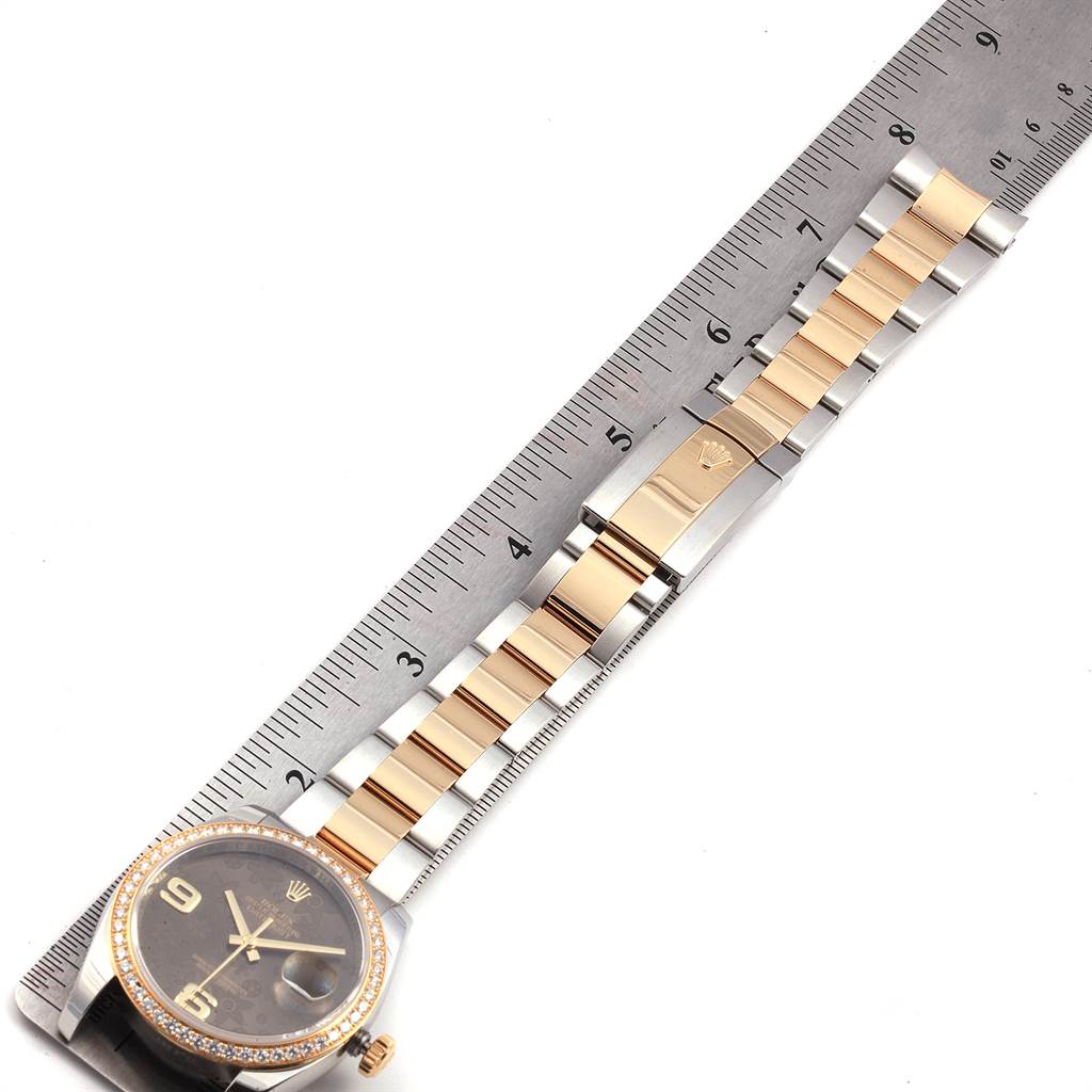 The Rolex Datejust 116243 Women's Steel and Gold (two tone) Brown Dial 116243 Women's Steel and Gold (two tone) Brown Dial watch is shown from an overhead angle, featuring its face, bezel, and metal band next to a ruler.