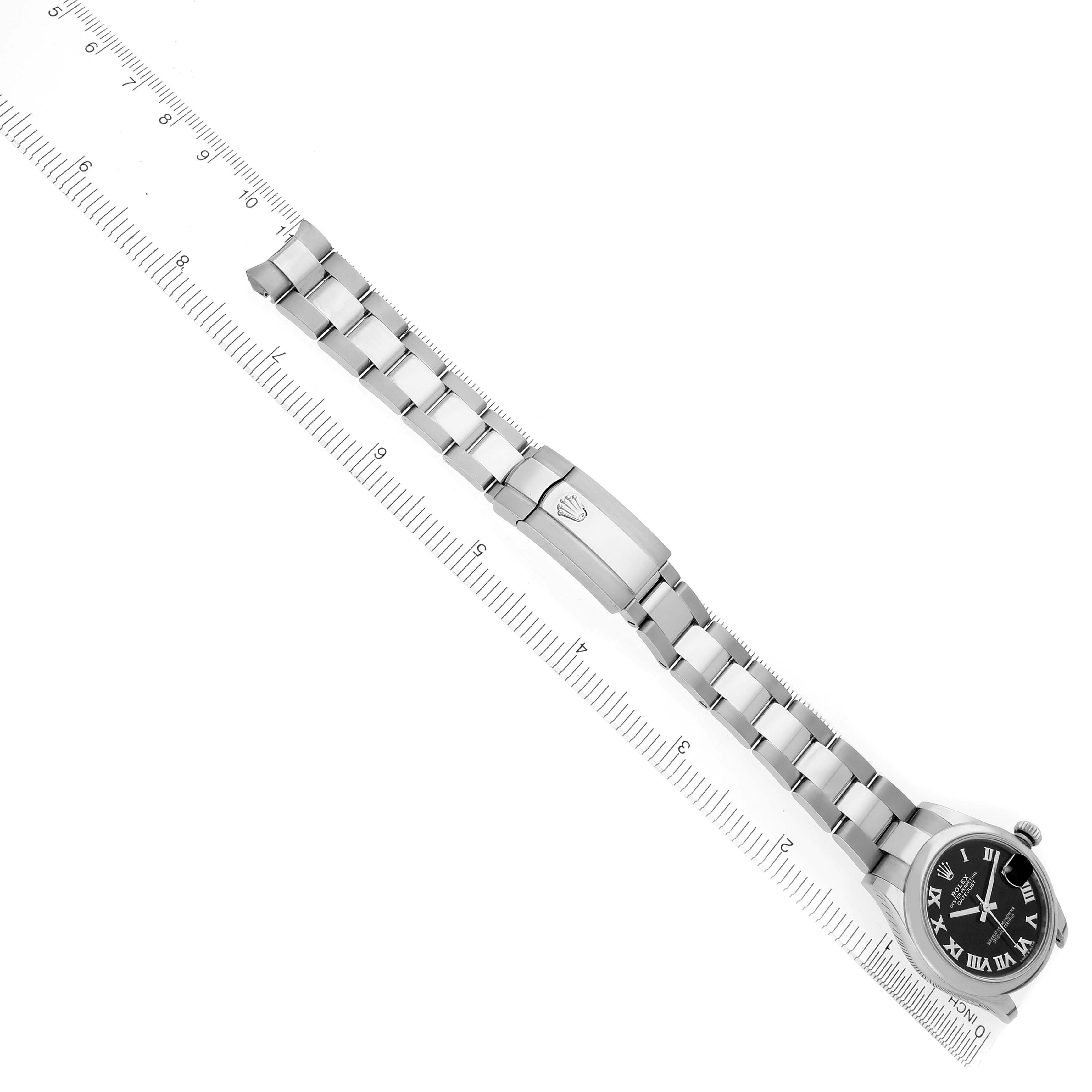The Rolex Datejust watch is shown at an overhead angle, highlighting the black dial, bracelet, and clasp next to a ruler.
