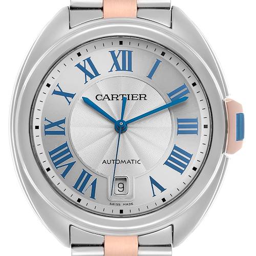 The Cartier Clé watch is shown from a top-down angle, highlighting its dial, blue Roman numerals, and date window.