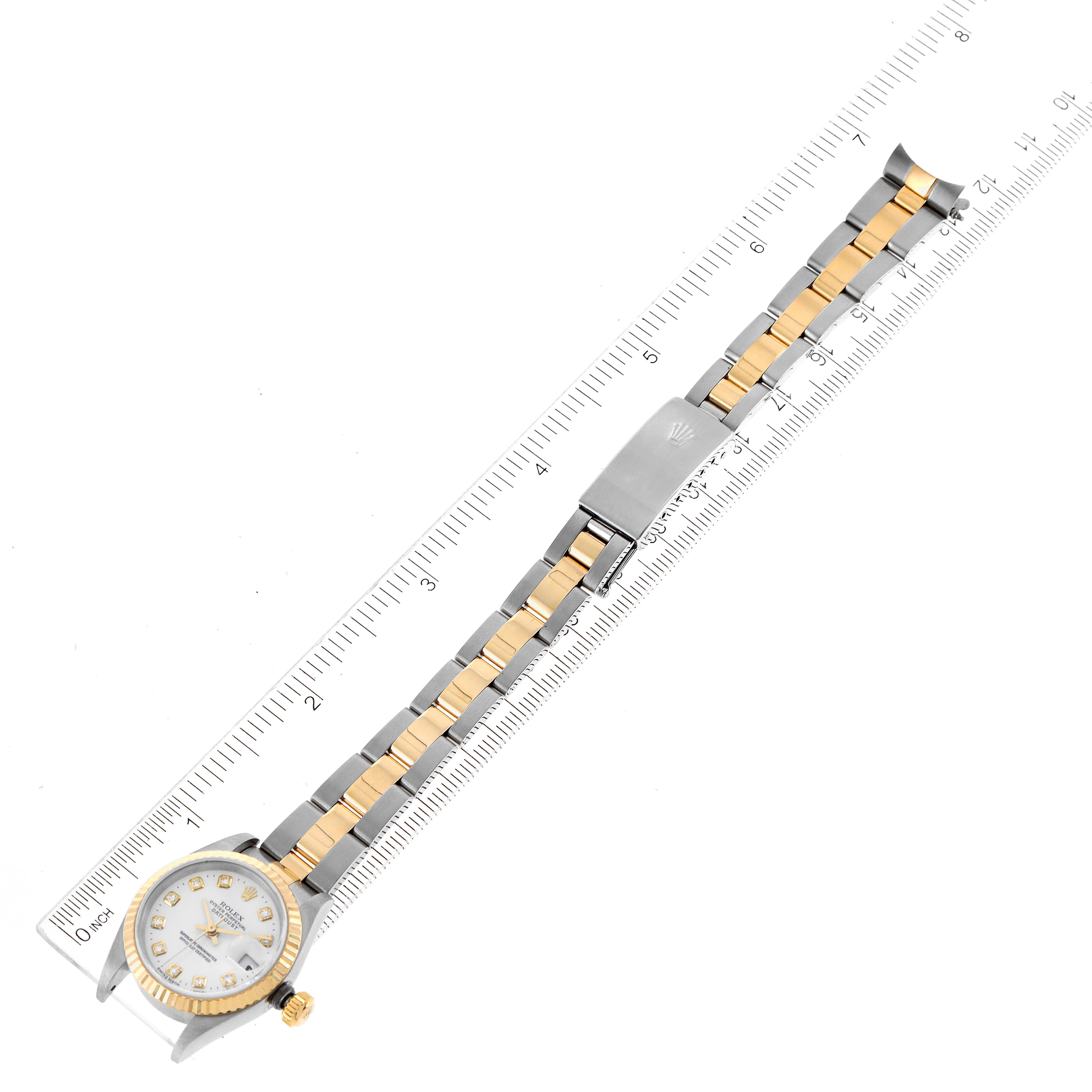 The image shows a Rolex Datejust 79173 Women's Steel and Gold (two tone) White Dial 79173 Women's Steel and Gold (two tone) White Dial watch placed on a ruler, displaying the face, bracelet, and clasp from a top-down angle.