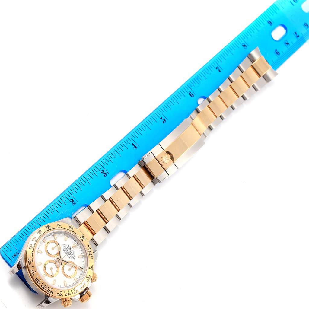 The image shows a Rolex Daytona 116503 Men's Steel and Gold (two tone) White Dial 116503 Men's Steel and Gold (two tone) White Dial watch placed next to a blue ruler, capturing the face and entire band.