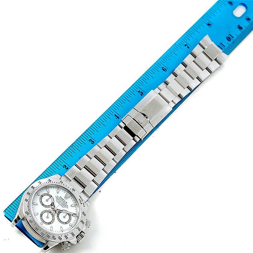 The image shows the entire Rolex Daytona 116520 Men's Stainless Steel White Dial 116520 Men's Stainless Steel White Dial watch, including the face, bezel, and bracelet, laid next to a blue ruler.