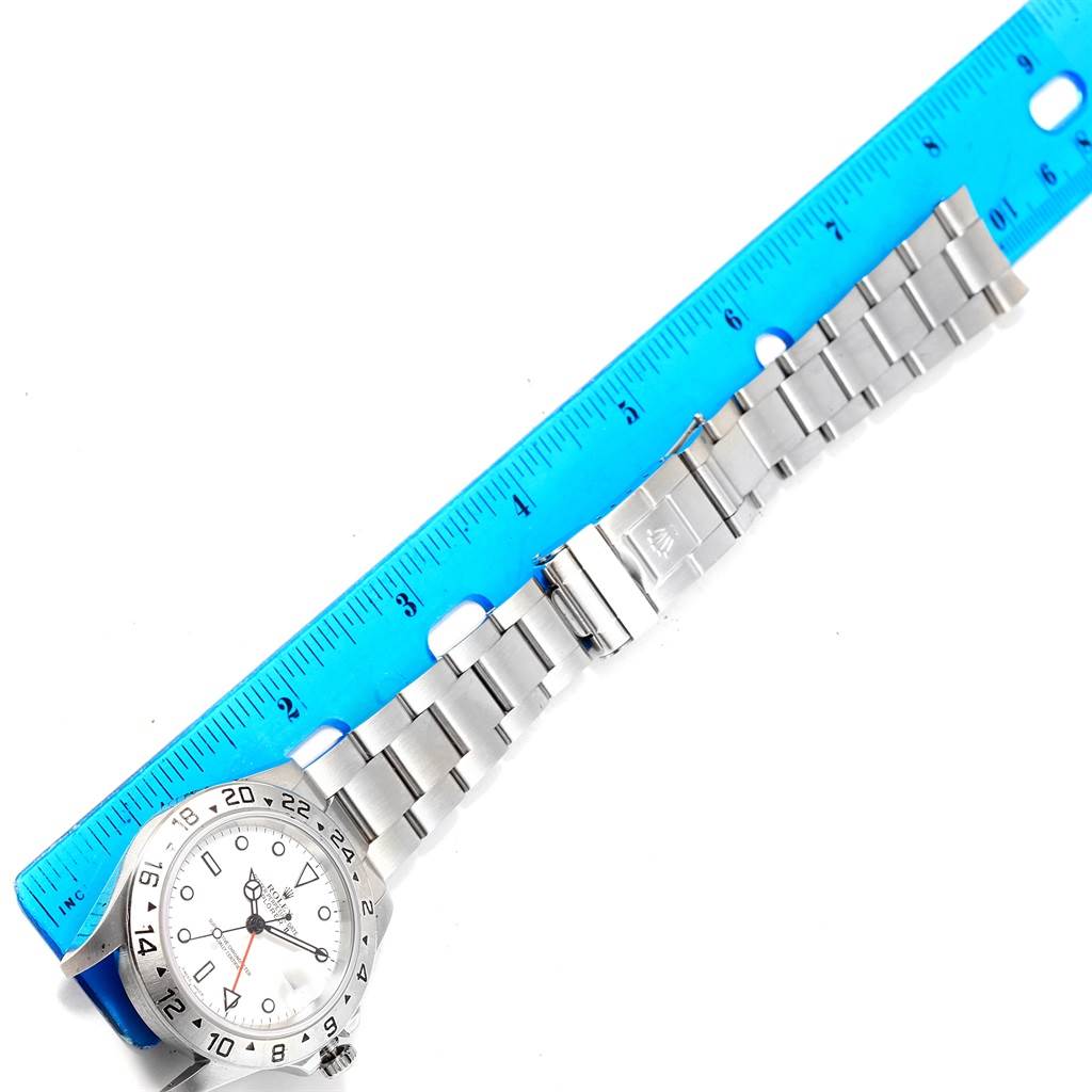 The image shows the front view of a Rolex Explorer 16570 Men's Stainless Steel White Dial 16570 Men's Stainless Steel White Dial watch with its stainless steel bracelet aligned next to a blue ruler.