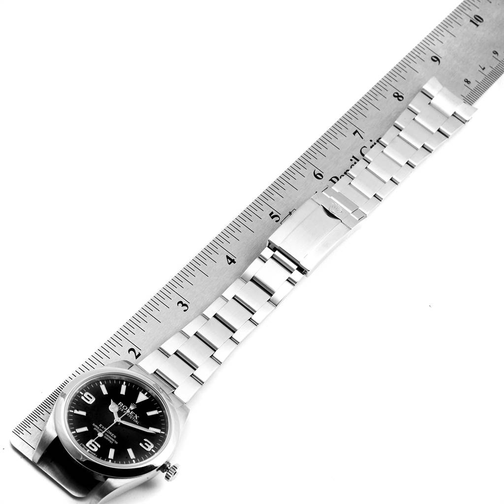 The image shows the Rolex Explorer 214270 Men's Stainless Steel Black Dial 214270 Men's Stainless Steel Black Dial watch laid flat alongside a ruler, displaying the watch face and the entire metal bracelet.