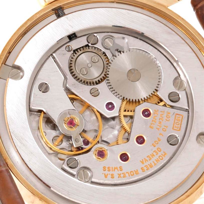 The image shows the inner mechanism of a Rolex Cellini 5115 Men's Yellow Gold Beige Dial 5115 Men's Yellow Gold Beige Dial watch, featuring gears, jewels, and the movement components.