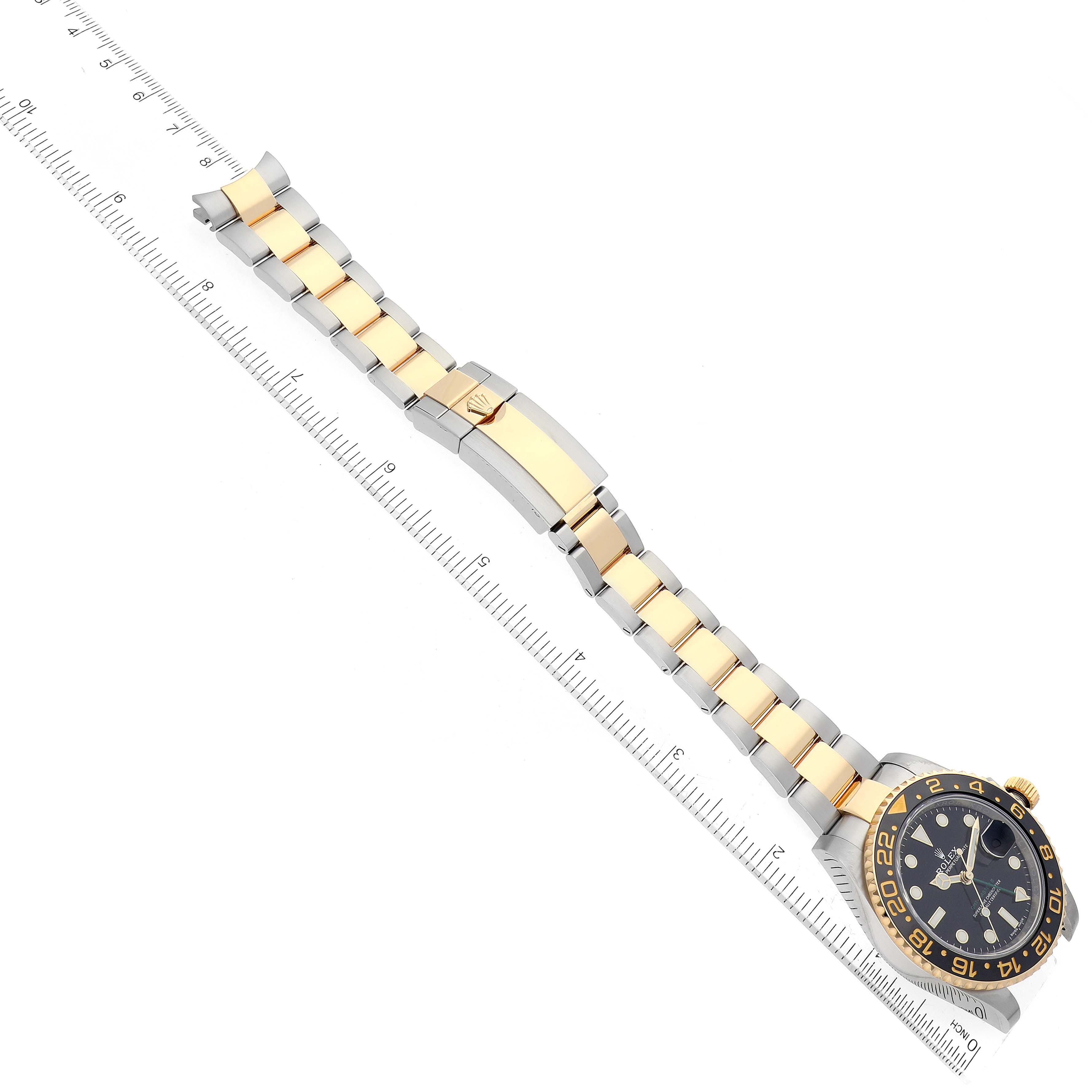The image shows a top-down view of the Rolex GMT-Master 116713 Men's Steel and Gold (two tone) Black Dial 116713 Men's Steel and Gold (two tone) Black Dial watch including its face and bracelet next to a ruler.