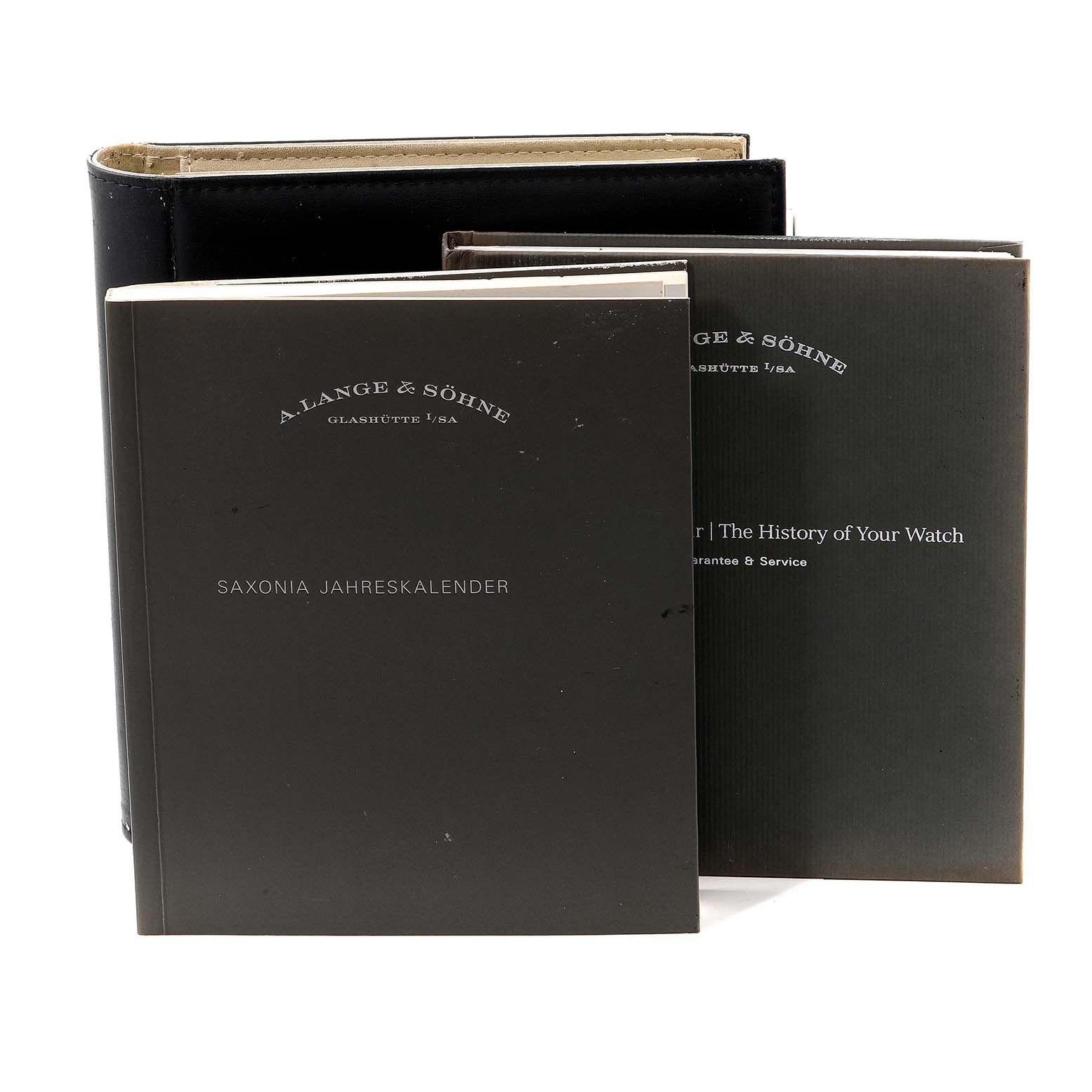 The image shows manuals and booklets for the A. Lange & Sohne Saxonia 330.032 Men's Rose Gold Silver Dial watch model.