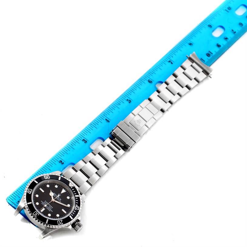 The Rolex Submariner 14060 Men's Stainless Steel Black Dial 14060 Men's Stainless Steel Black Dial watch is shown lying flat with its metal bracelet and clasp fully extended next to a ruler for measurement.