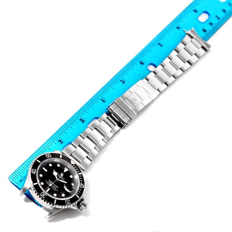 This image shows a Rolex Submariner 16610 Men's Stainless Steel Black Dial 16610 Men's Stainless Steel Black Dial watch laid flat on a surface with a blue ruler for scale, displaying the full bracelet and face.