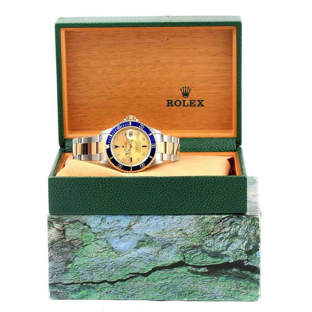 The image shows a Rolex Submariner 16613 Men's Steel and Gold (two tone) Champagne Dial 16613 Men's Steel and Gold (two tone) Champagne Dial watch with a gold dial and blue bezel, presented in an open green and wood Rolex box.