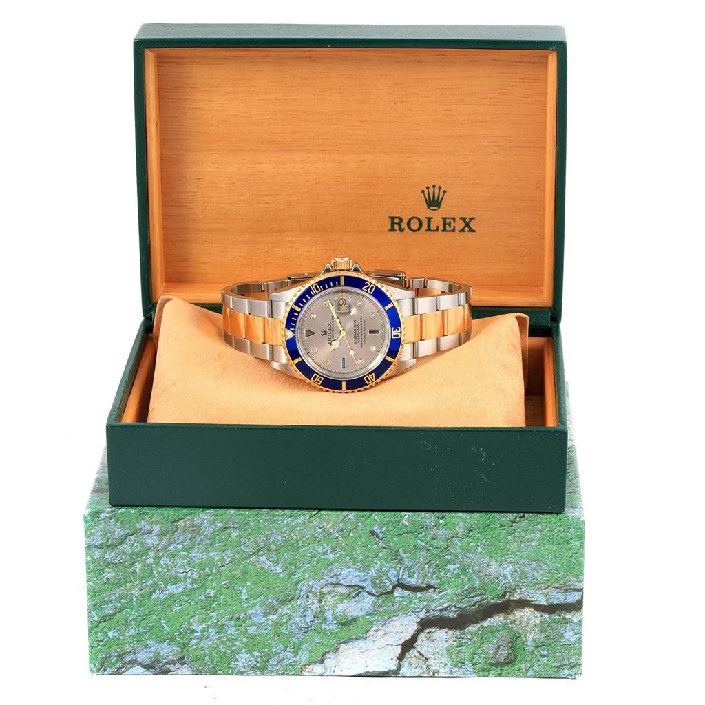 The Rolex Submariner 16613 Men's Steel and Gold (two tone) Grey Dial 16613 Men's Steel and Gold (two tone) Grey Dial watch is shown from the front placed in an open green and beige Rolex box.
