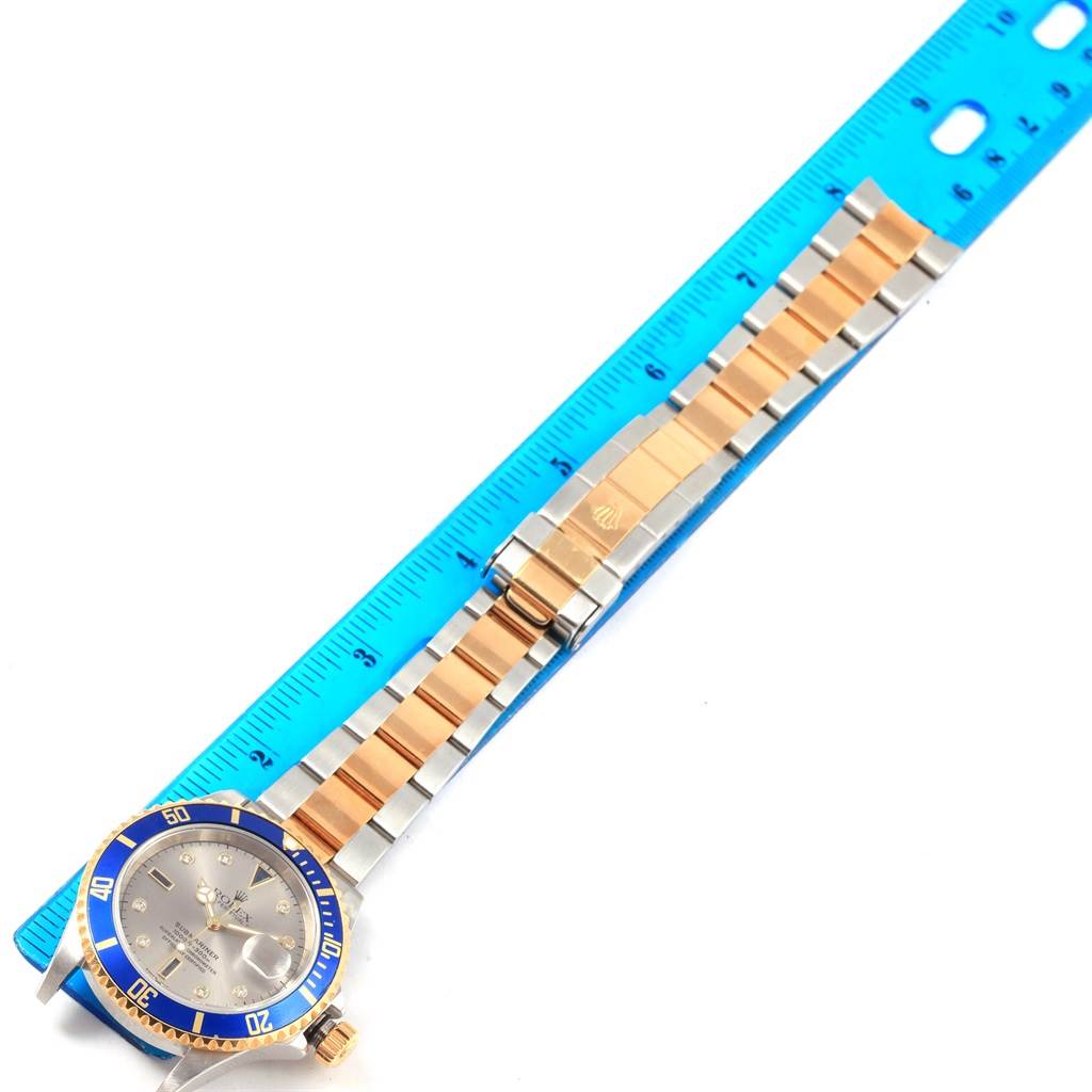 The image shows a Rolex Submariner 16613 Men's Steel and Gold (two tone) Grey Dial 16613 Men's Steel and Gold (two tone) Grey Dial watch laid flat with a blue ruler, highlighting the face, bezel, band, and clasp.