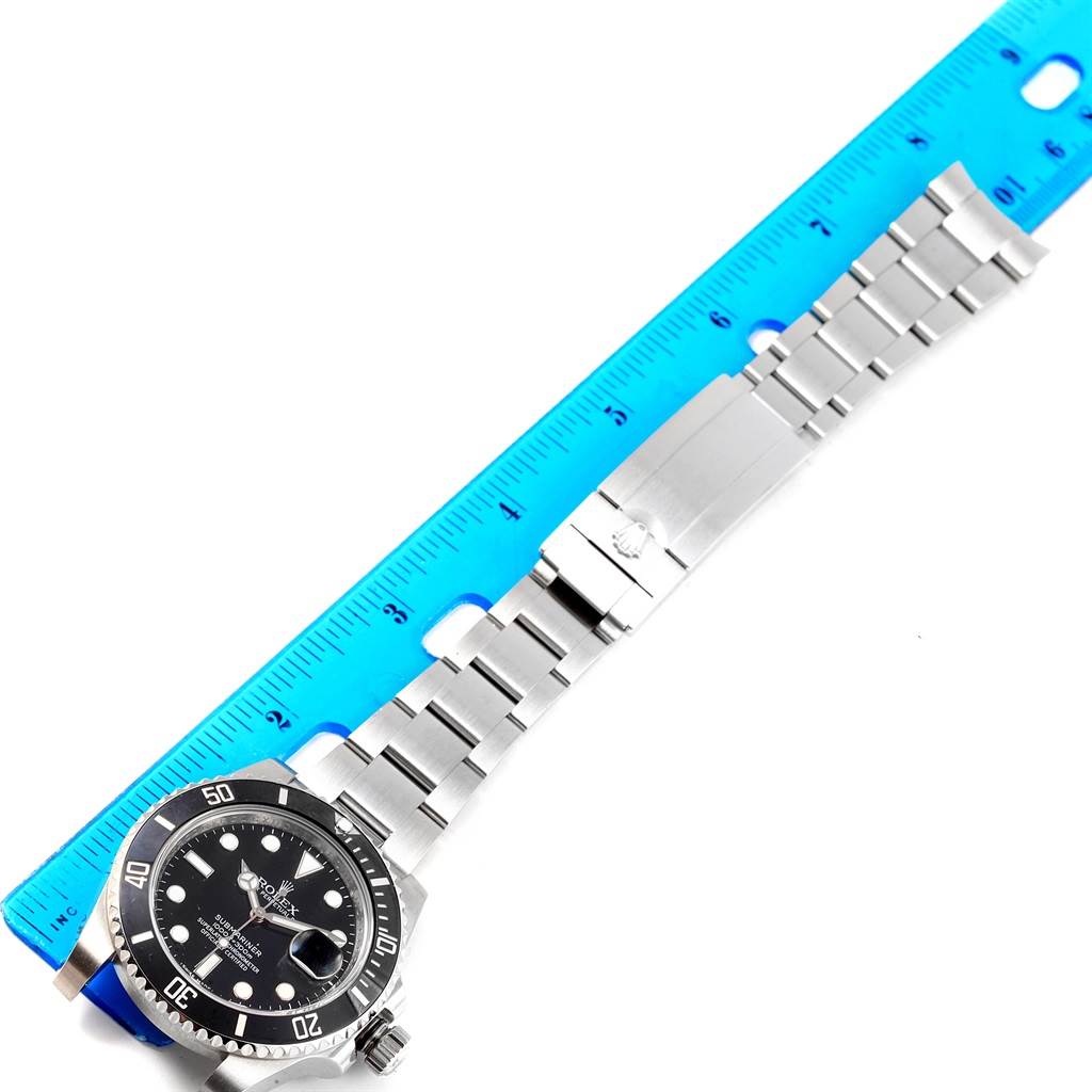 The image shows a Rolex Submariner 116610 Men's Stainless Steel Black Dial 116610 Men's Stainless Steel Black Dial watch laid flat with a blue ruler beside it, displaying the watch face and stainless steel bracelet.