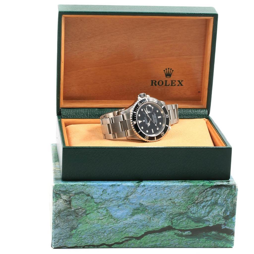 The Rolex Submariner 16610 Men's Stainless Steel Black Dial 16610 Men's Stainless Steel Black Dial watch is displayed at a slight angle within its open green and wood box.
